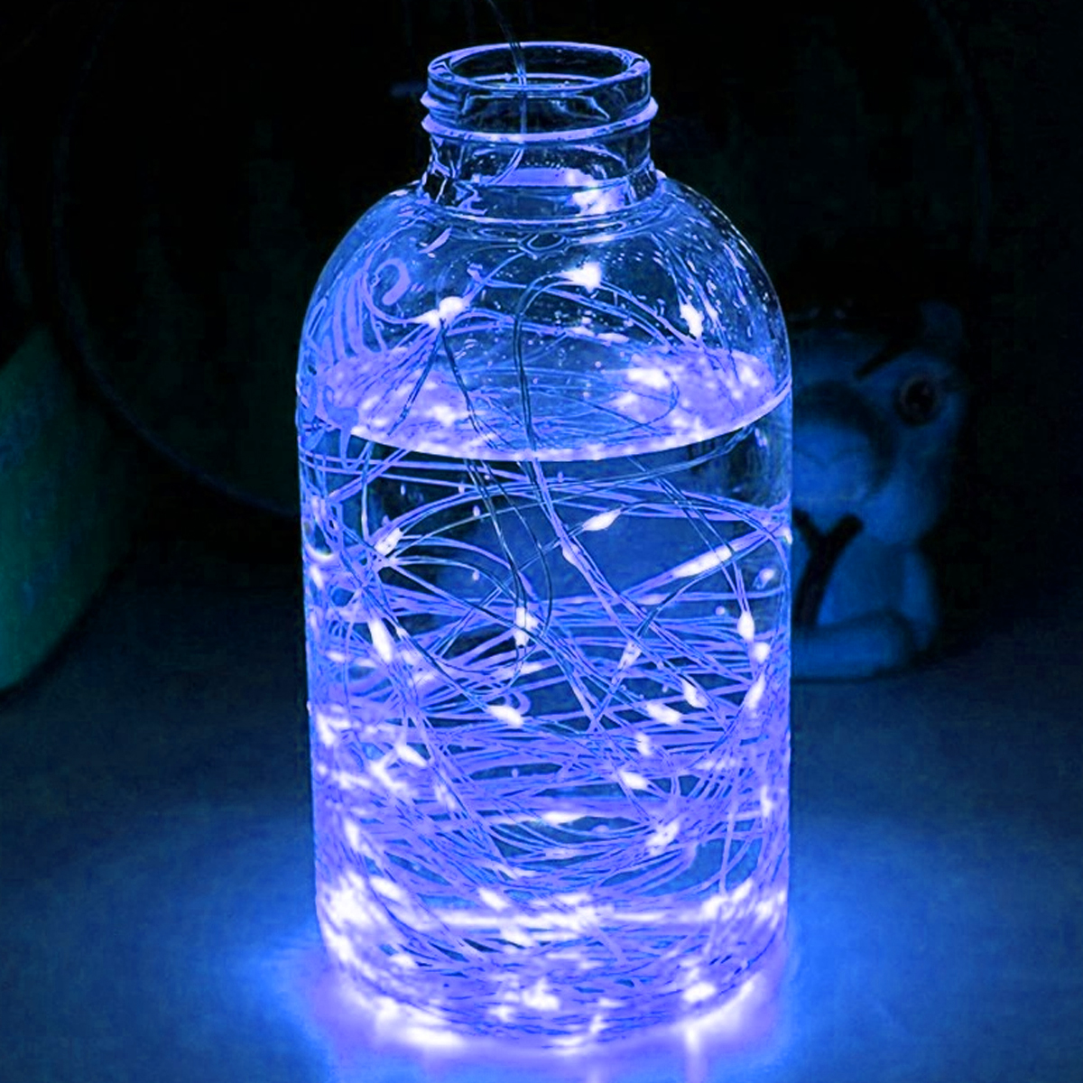Ein Glasgefäß mit Wasser und blauen Lichterketten. Das Gefäß steht auf einer blauen Oberfläche, mit dunklem Hintergrund.