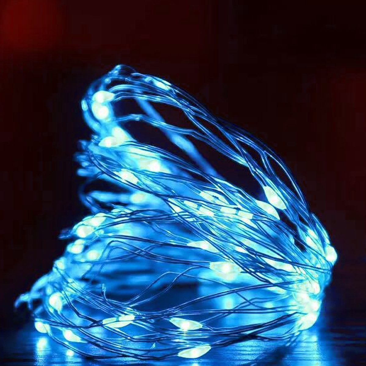 Nahaufnahme von blauen Lichterketten. Die Lichter sind an einem dünnen Draht, der Hintergrund ist dunkelrot.