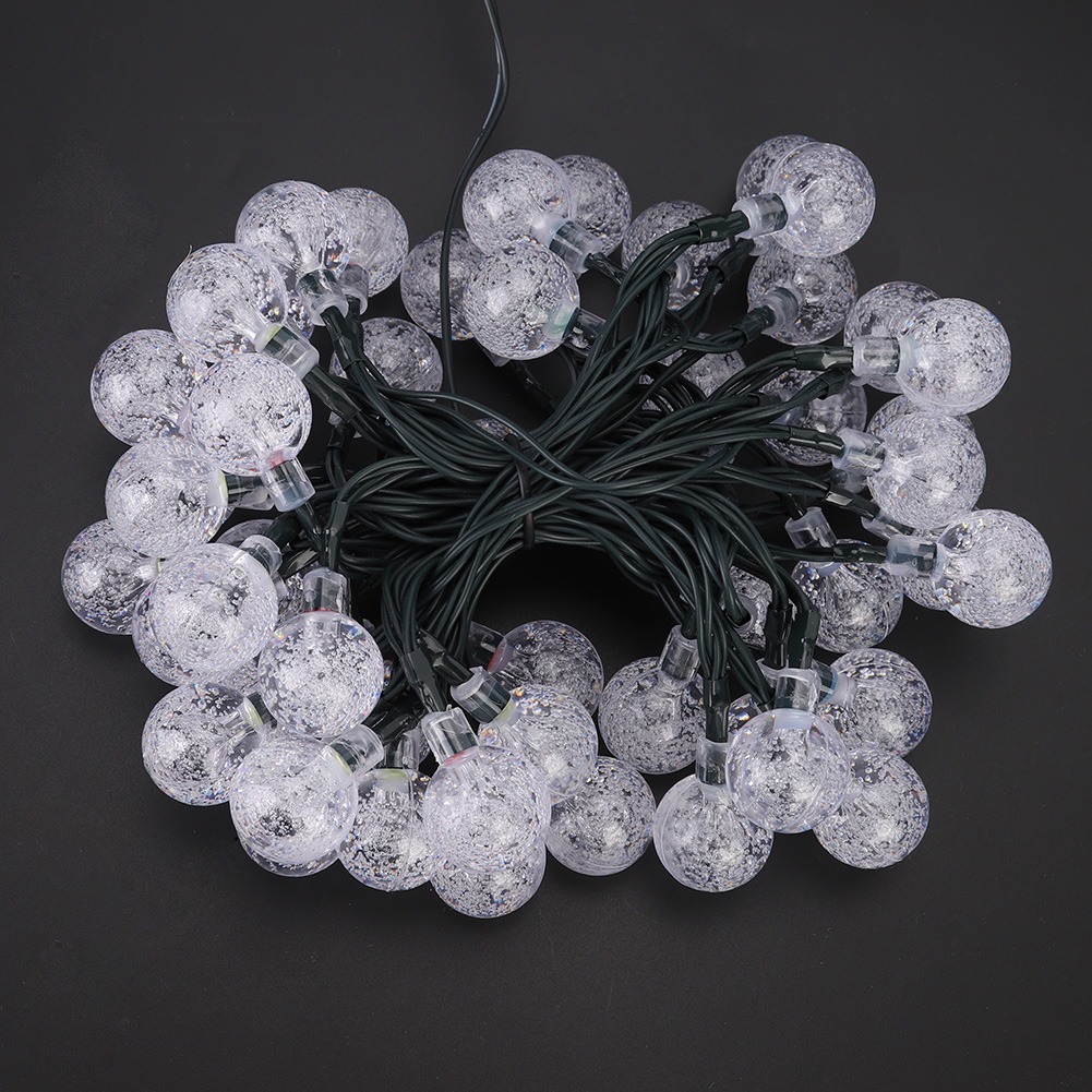 Luci a stringa con lampadine sferiche trasparenti su sfondo nero. Filo verde che collega le lampadine. Le lampadine hanno un aspetto strutturato.