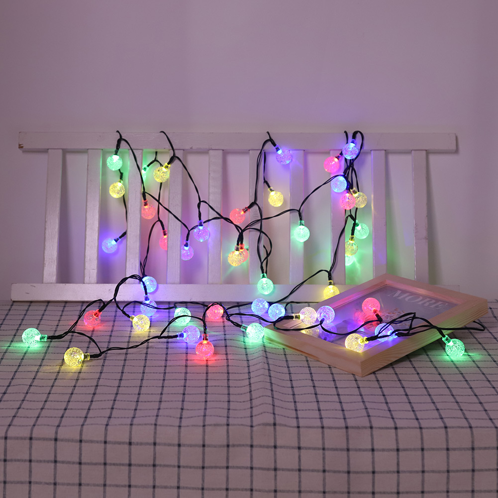 Stringa di luci con lampadine colorate su un tavolo con testiera bianca e cornice. Il tavolo è coperto da un panno a quadri.