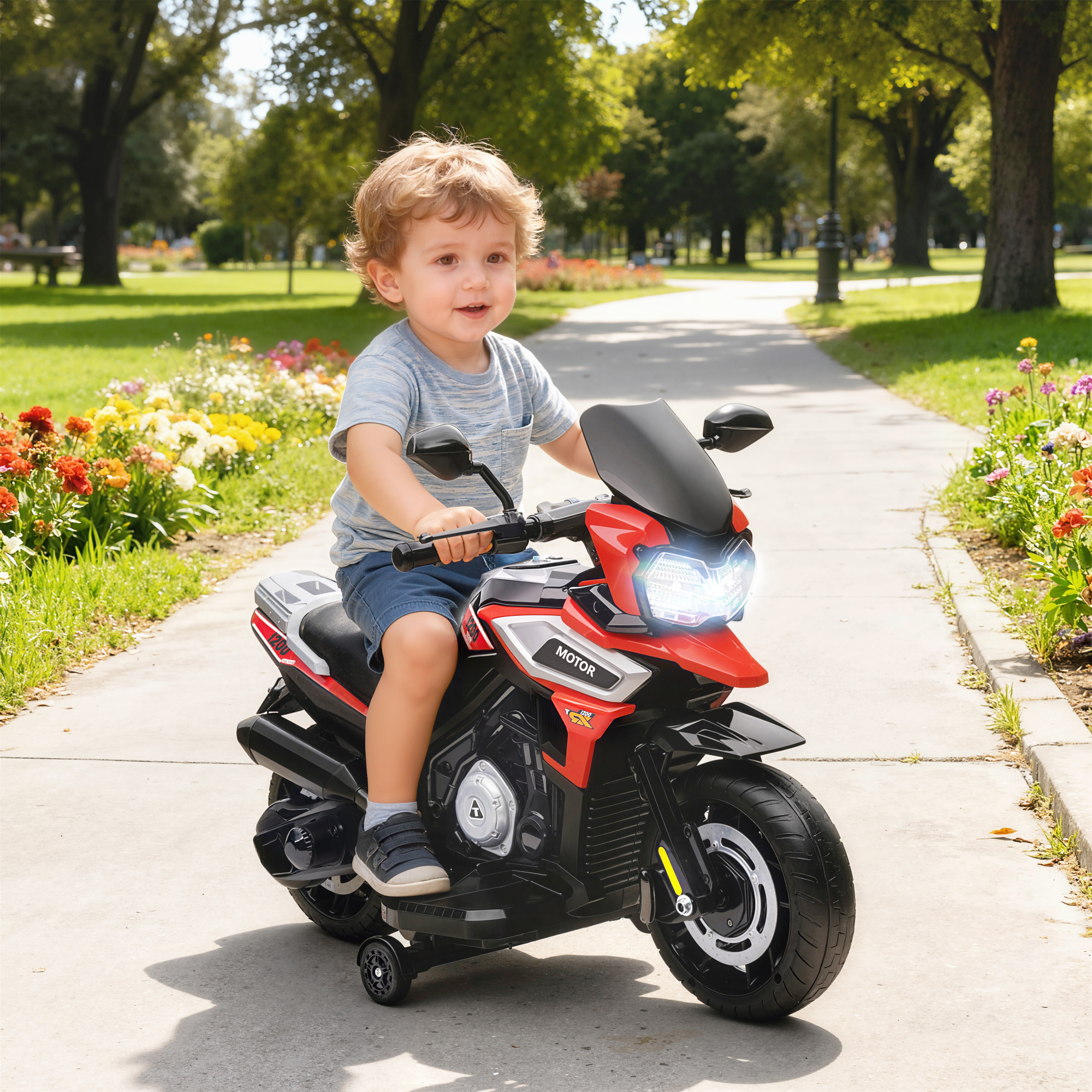 Un ragazzino guida una moto giocattolo rossa e nera su un sentiero pavimentato in un parco, sorridendo. Fiori e alberi sullo sfondo.