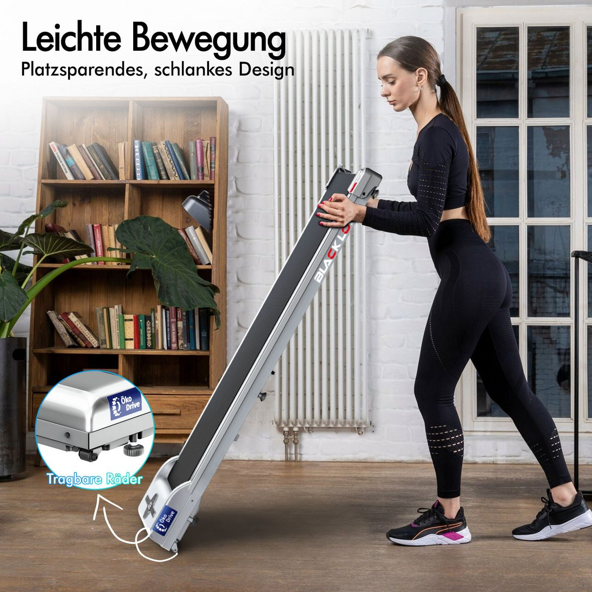Eine Frau in schwarzer Sportkleidung schiebt ein Laufband. Es befindet sich in einem Raum mit Bücherregal, Heizkörper und Fenster.