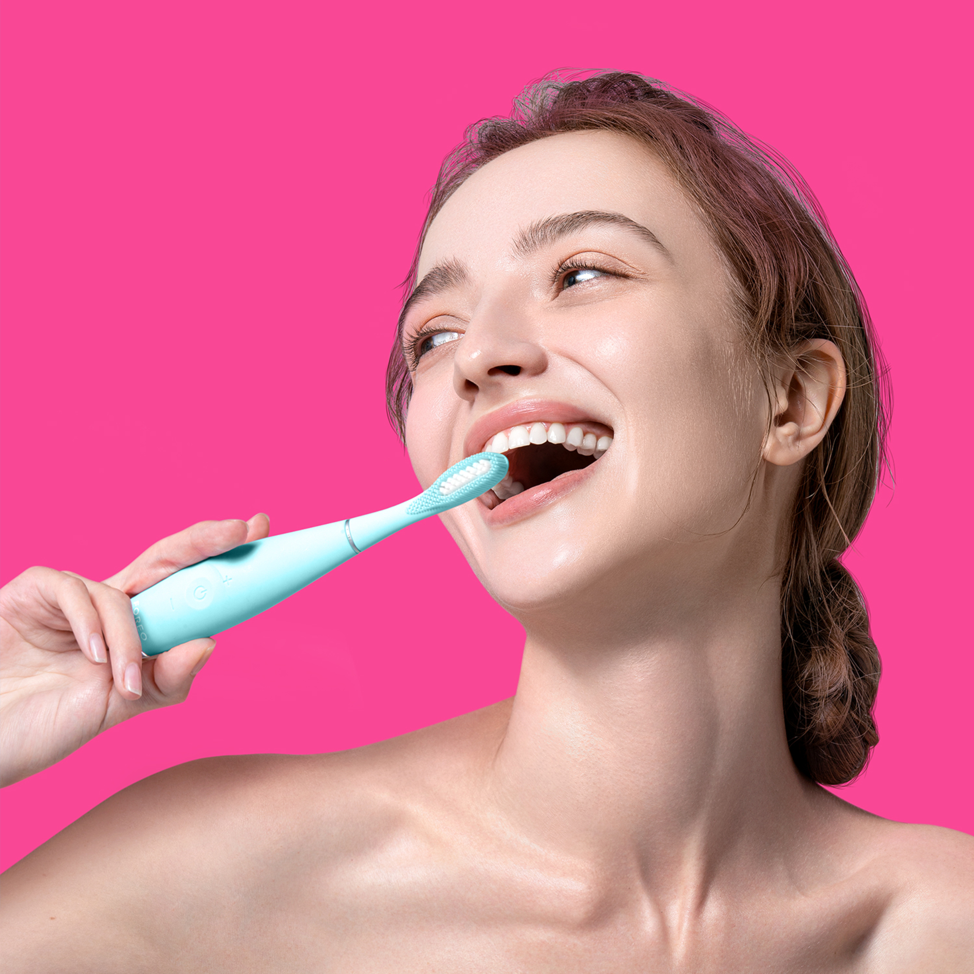 Una mujer se cepilla los dientes con un cepillo de dientes eléctrico azul. Fondo rosa.