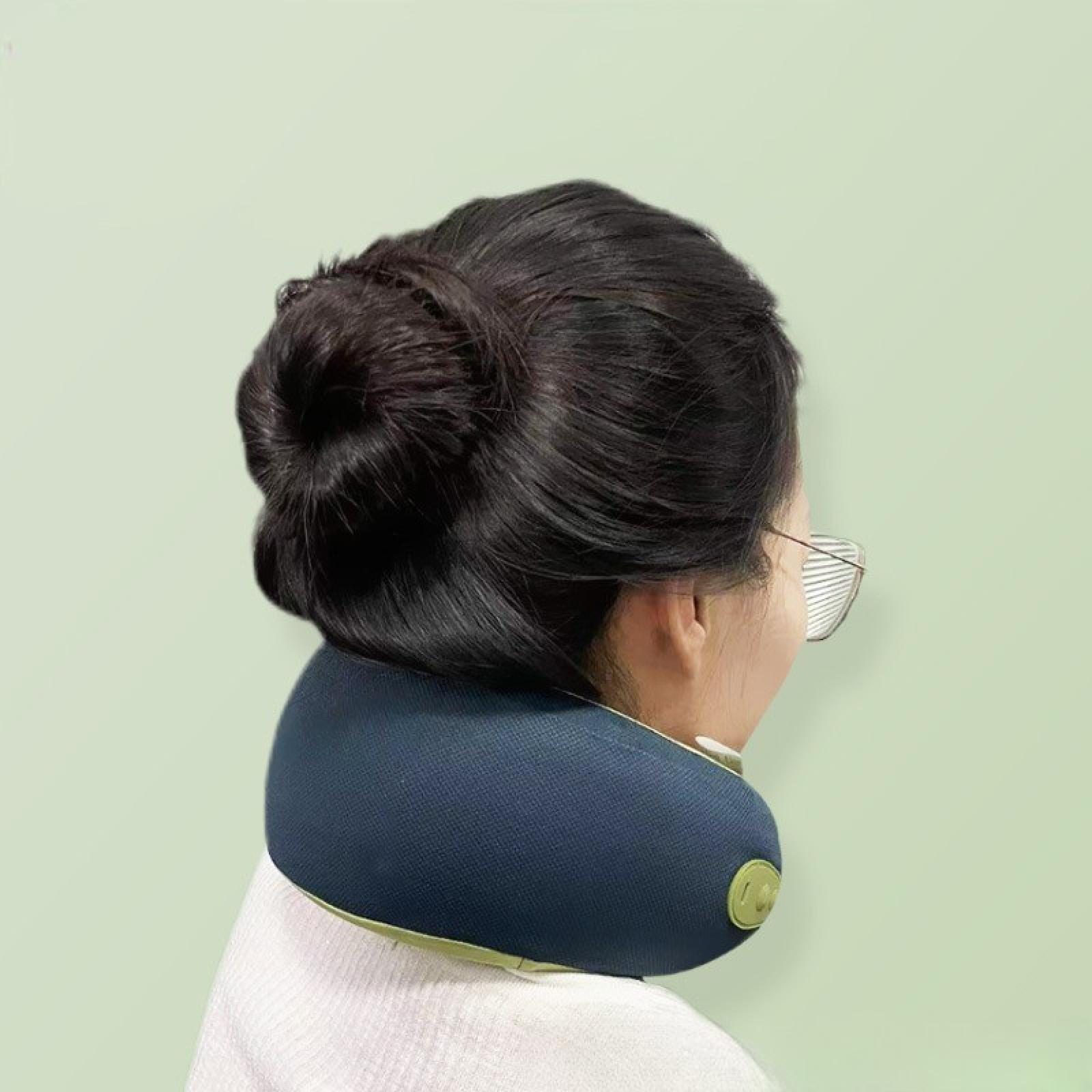 Eine Frau mit Brille und einem dunkelblauen Nackenmassagegerät, mit Haaren im Dutt, von hinten gesehen.