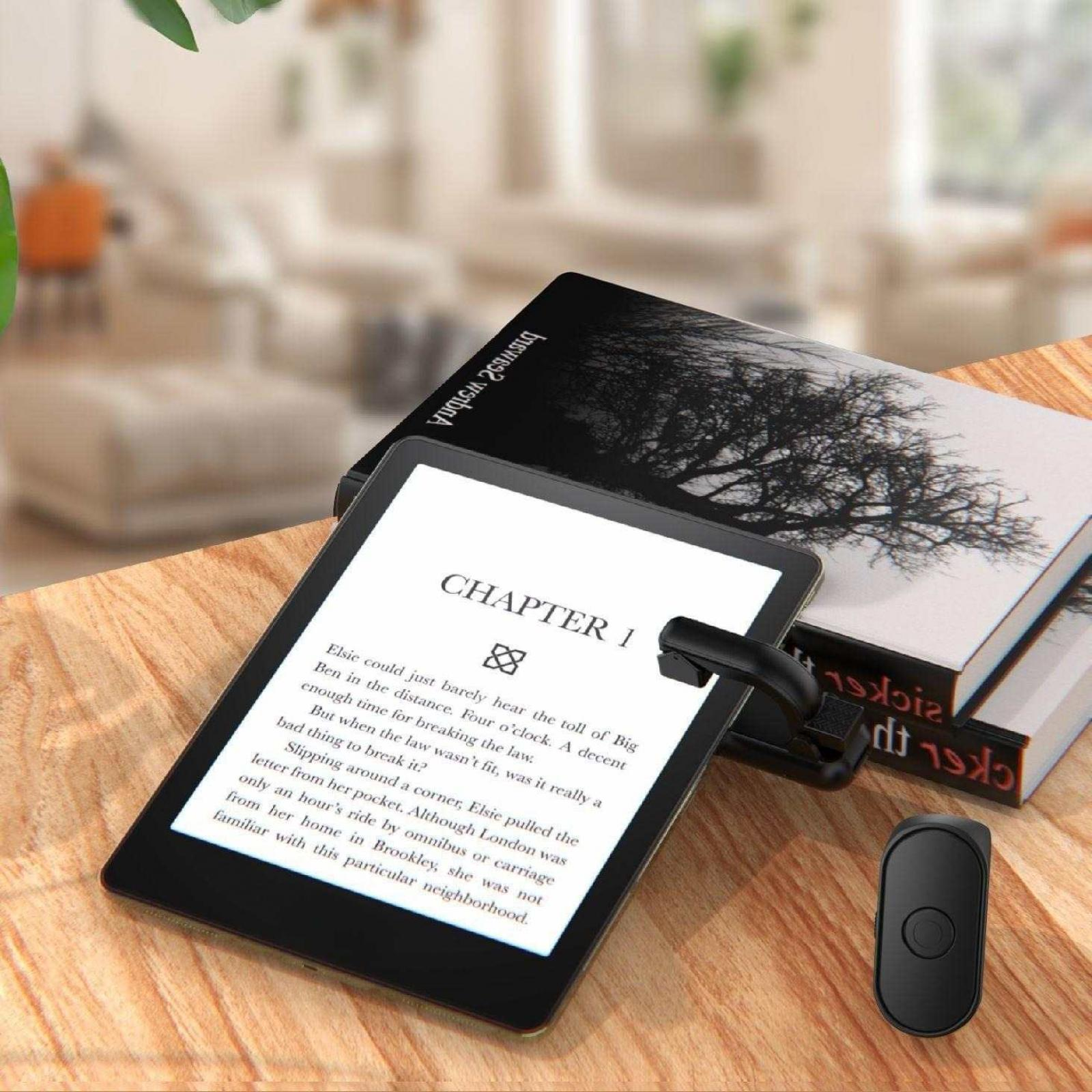 Ein E-Reader mit Leselicht und Fernbedienung sowie ein Buch mit Baumdesign auf einem Holztisch.