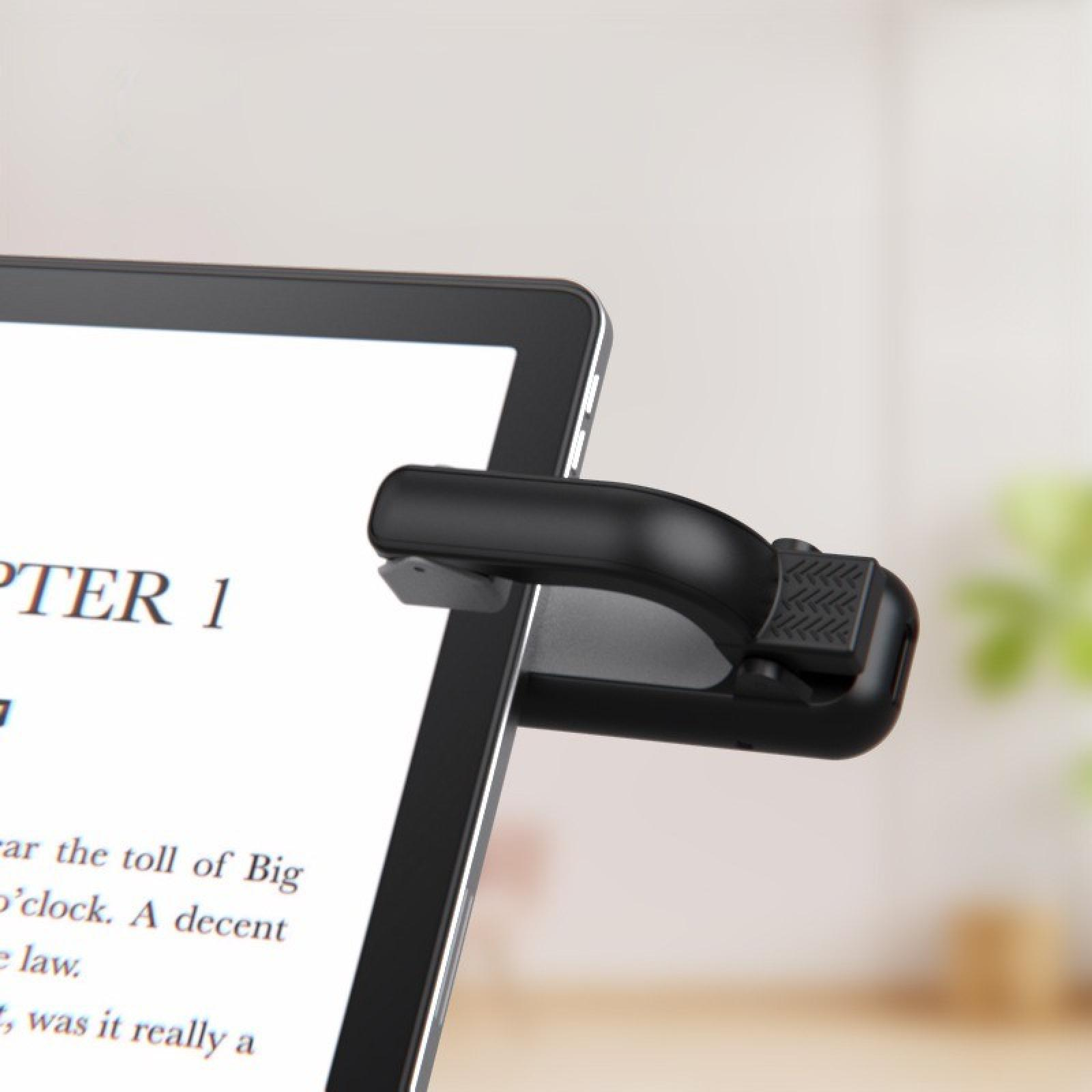 Ein schwarzes Tablet mit einer angebrachten Buchlampe, das Text anzeigt. Der Hintergrund ist verschwommen mit einer Pflanze.