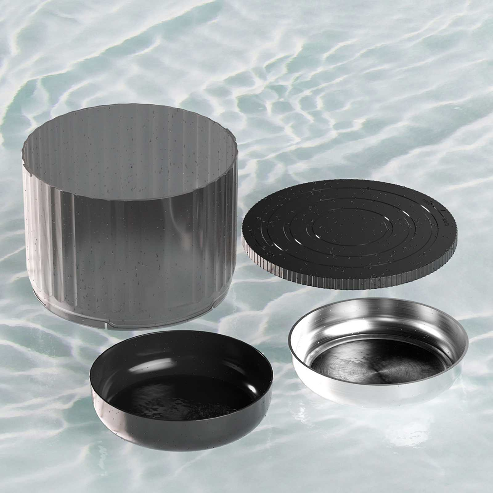 Ein zerlegter Behälter mit Deckel und zwei Schalen auf einer wasserartigen Oberfläche. Der Behälter ist grau, Schalen sind schwarz und silber.