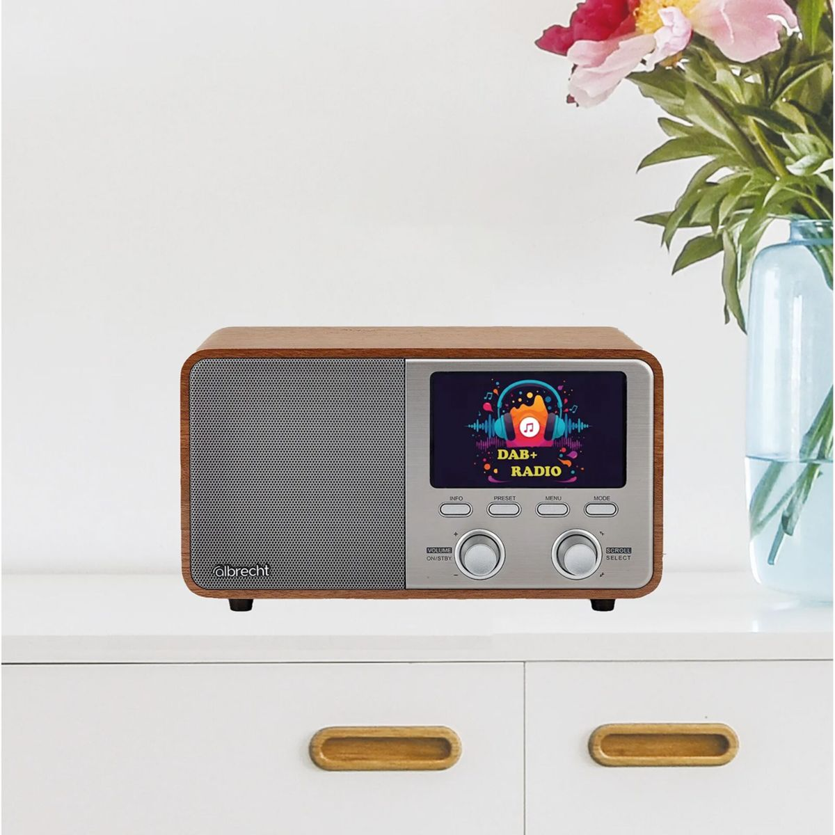 Una radio DAB+ in legno e argento su un mobile bianco. Fiori in un vaso sullo sfondo.