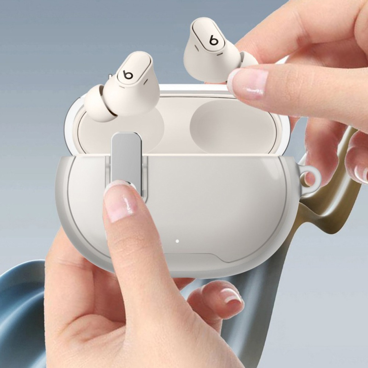 Hands holding white Beats earbuds and charging case. The case is open, revealing the earbuds inside. Blue background.