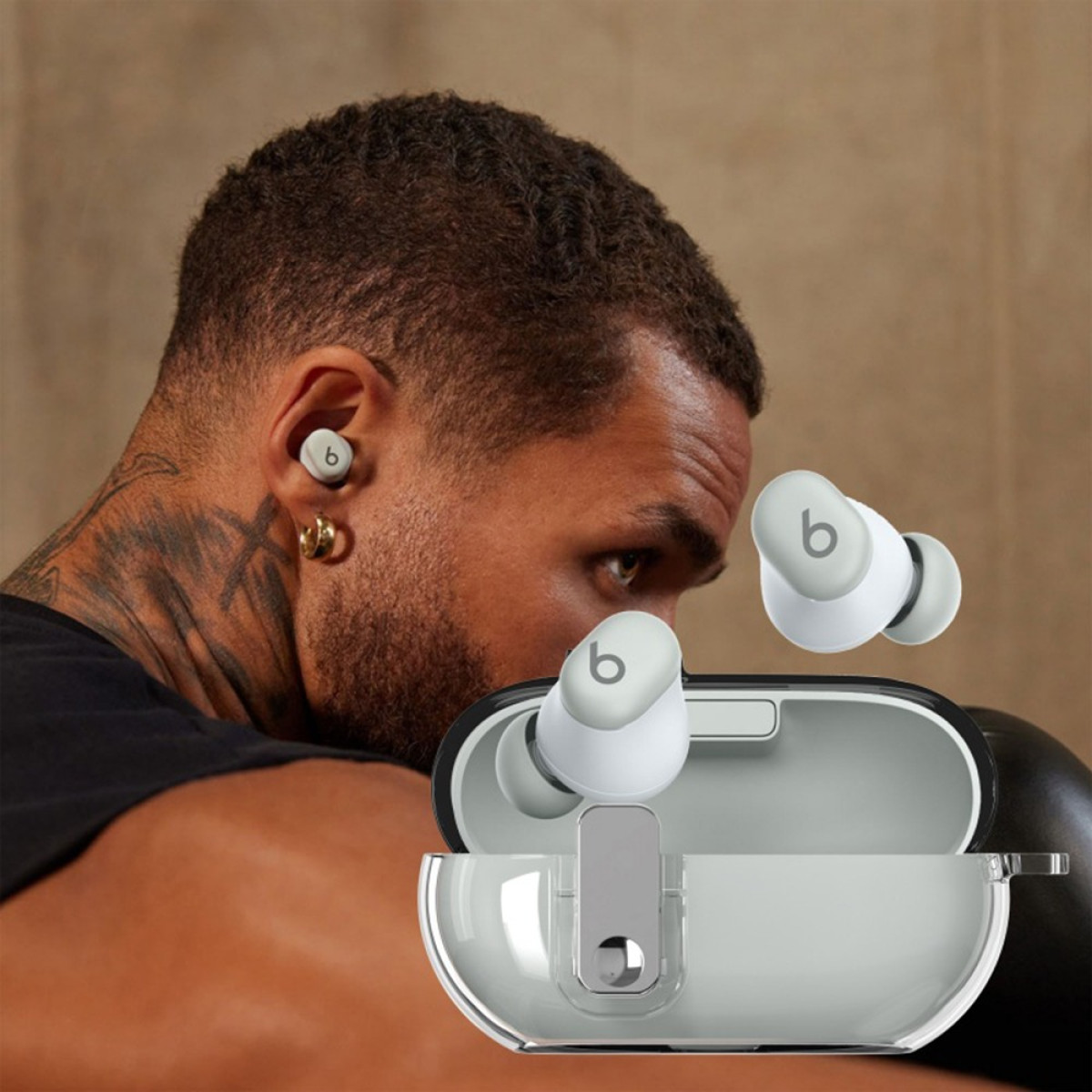 A man wearing an earbud is boxing. Earbuds and case are visible. The man has a neck tattoo and a gold earring.