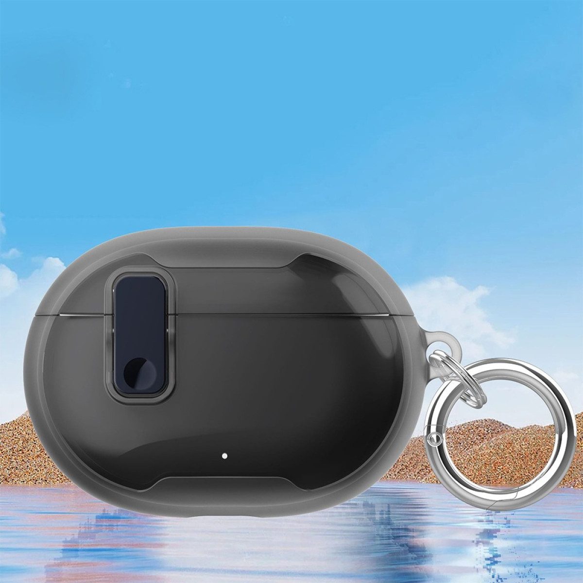 A dark gray earbud case with a silver keyring, set against a blue sky with water and sand in the background.