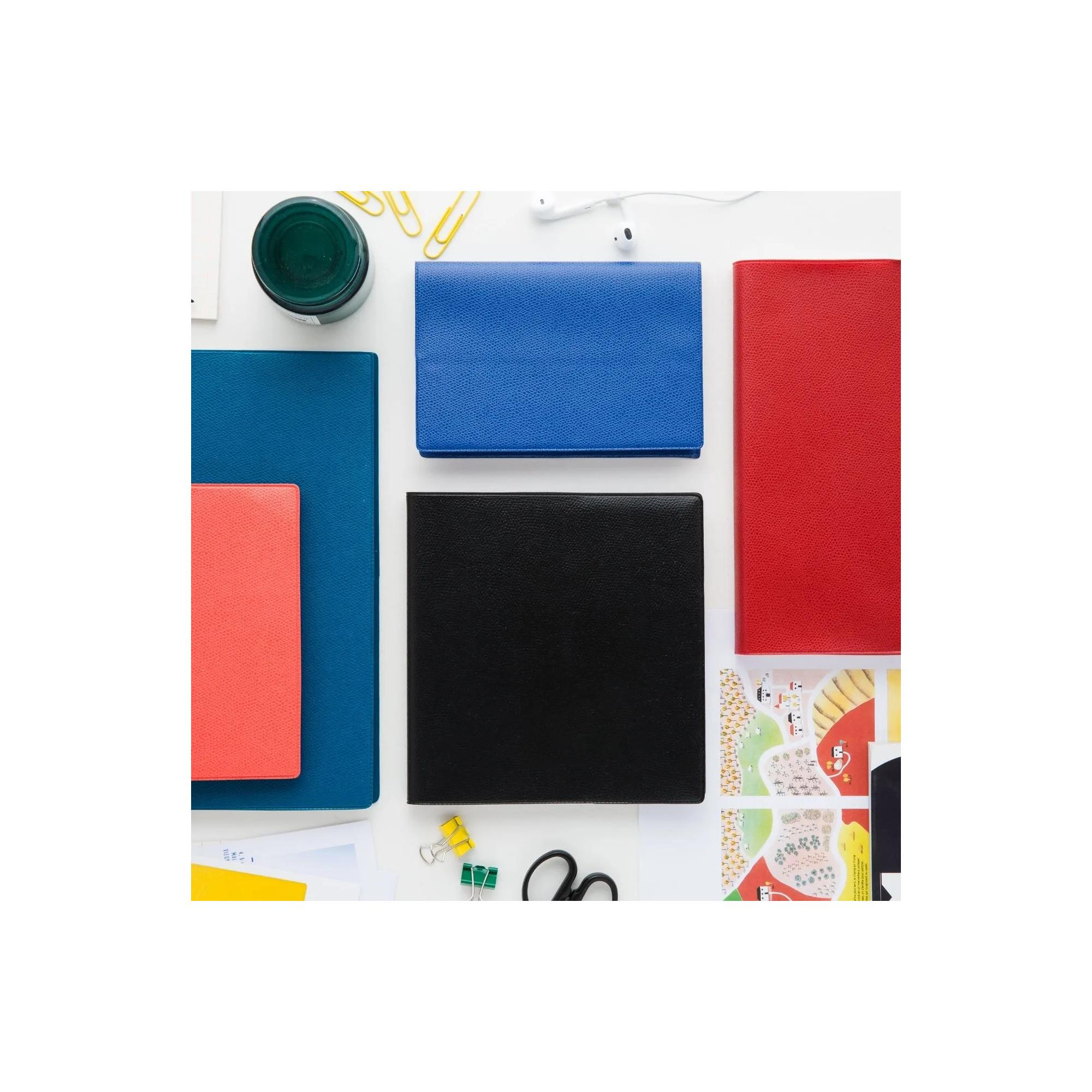Toma cenital de escritorio con cuadernos coloridos, auriculares y clips. Incluye cuadernos rojos, azules, negros y coral.