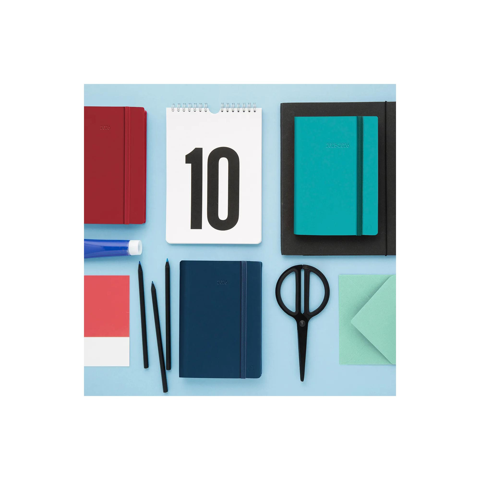 Vista cenital de artículos de papelería sobre fondo azul, incluyendo cuadernos, lápices, tijeras y un calendario con el número 10.