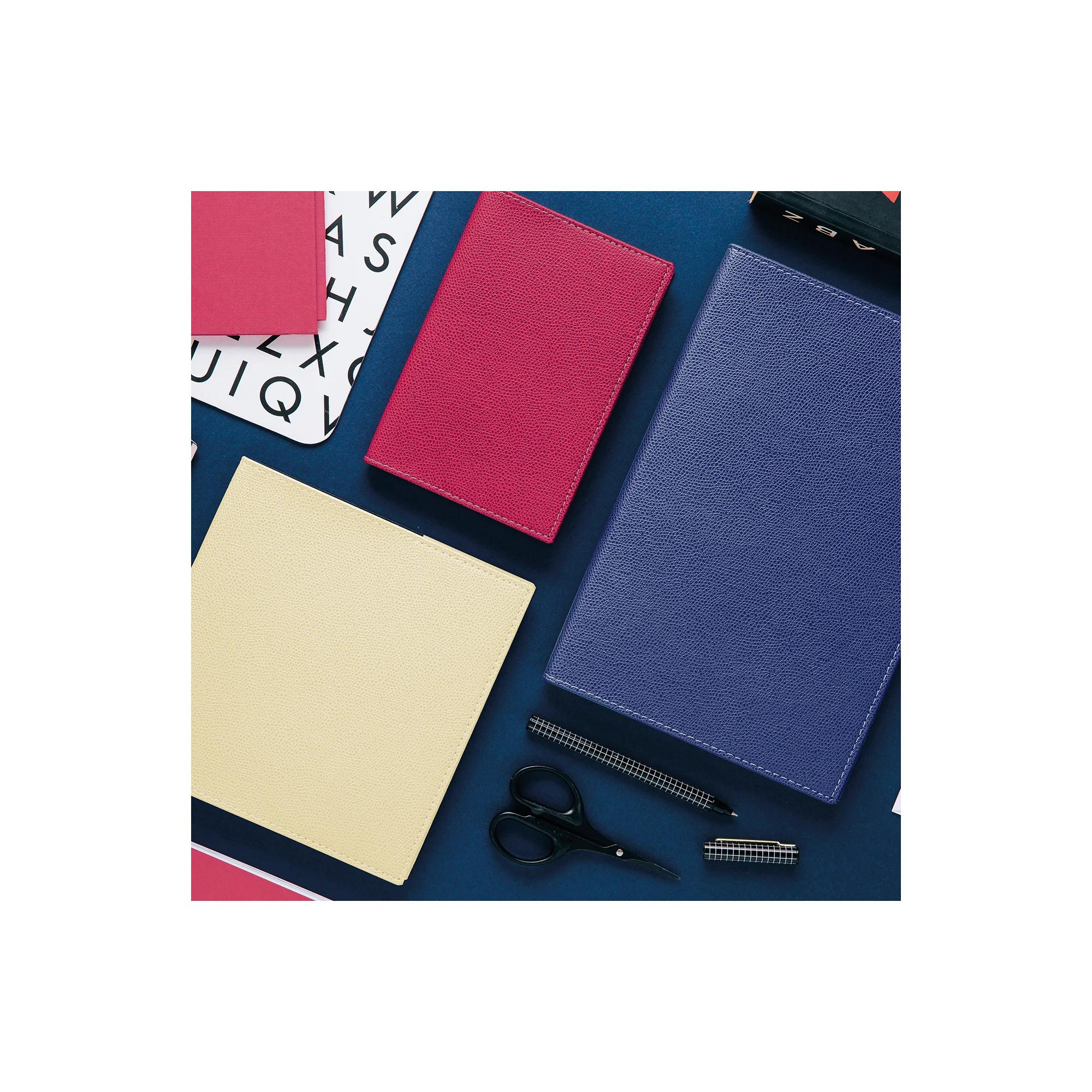 Cuadernos en rojo, rosa, azul y crema sobre una superficie azul. También hay tijeras y bolígrafos.