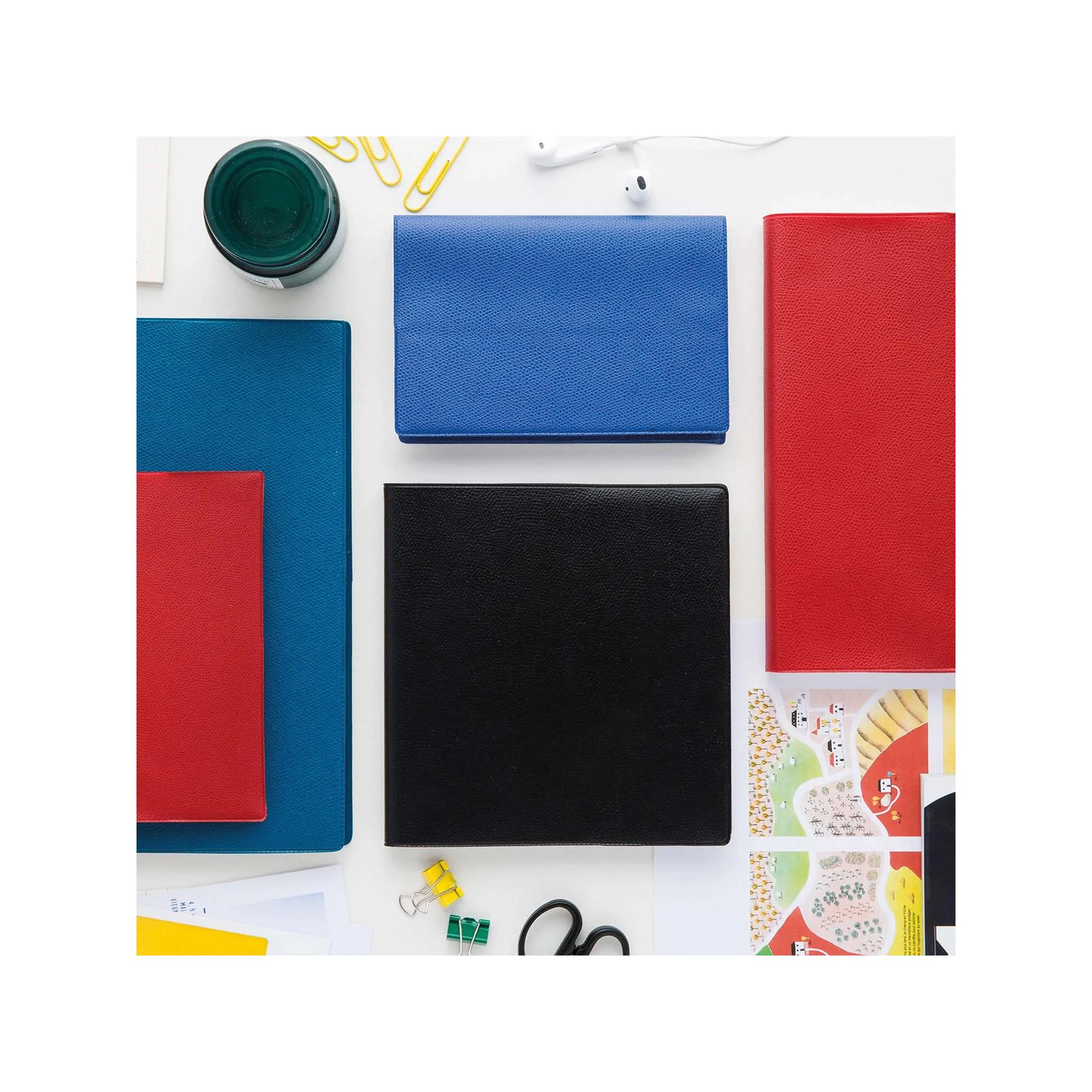 Toma cenital de cuadernos y artículos de papelería coloridos sobre una superficie blanca. Incluye cuadernos azules, rojos y negros, y accesorios.