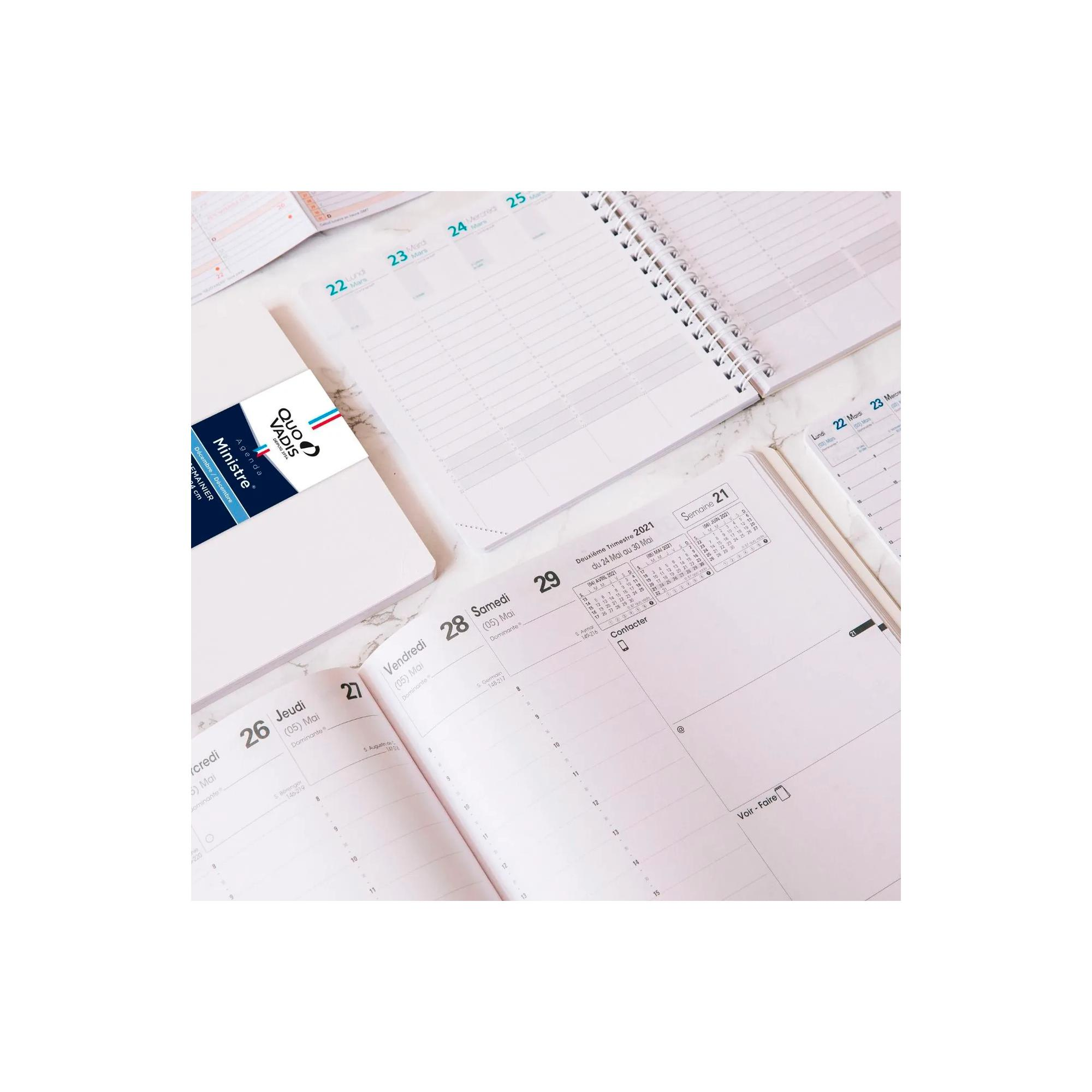Agenda abierta con portada blanca, algunas páginas abiertas. Fechas y días visibles. Tarjeta de visita a la izquierda.