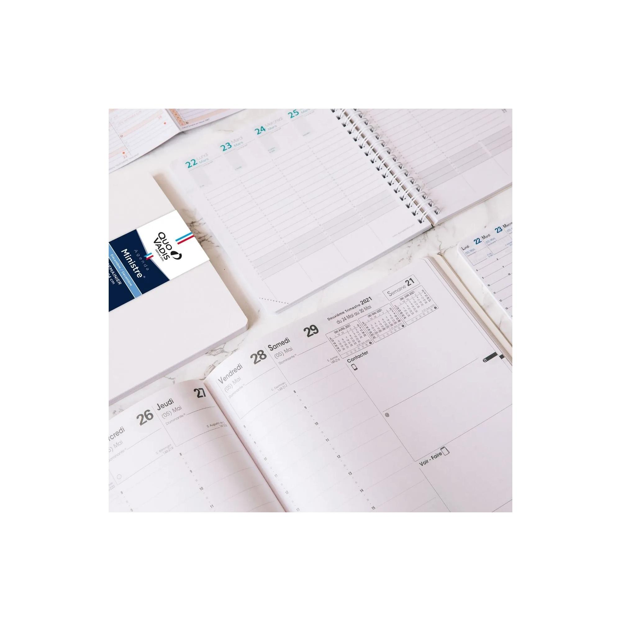 Agenda abierta con fechas, calendario y logotipo de Quo Vadis Ministre. Se ven los días de la semana. Páginas blancas y un bolígrafo.