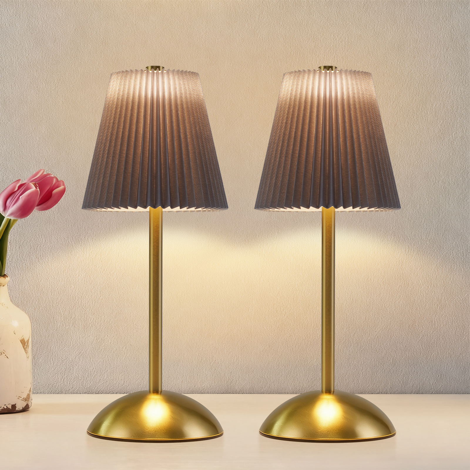 Due lampade dorate con paralumi grigi, un vaso di tulipani rosa a sinistra, e un muro bianco sullo sfondo.