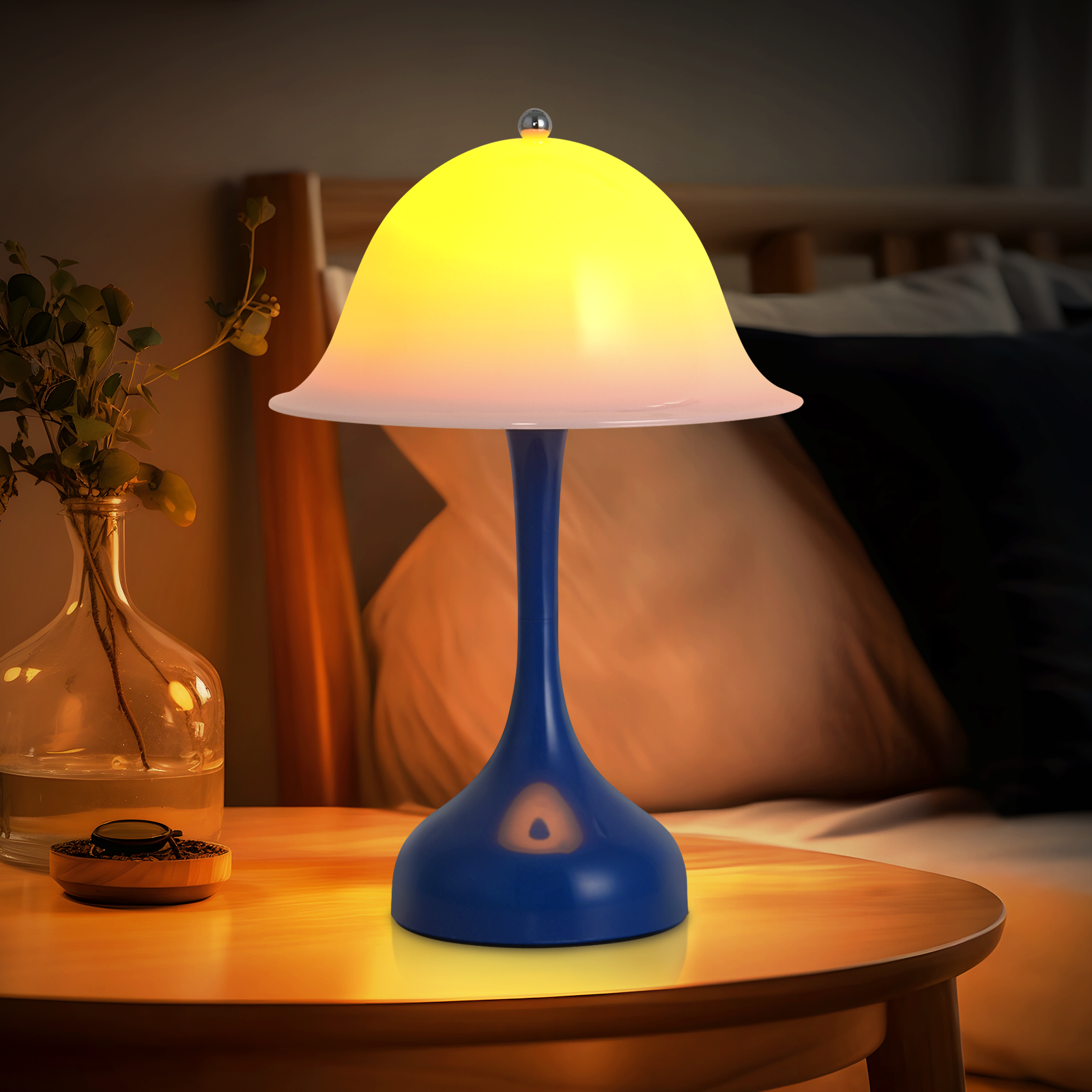 Una lampada blu con paralume giallo su un tavolo di legno. C'è anche un vaso con delle piante.