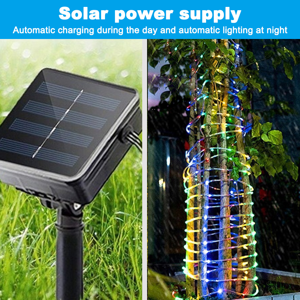 Solarpanel auf Gras, Kabel angeschlossen. Baum, der mit bunten Lichterketten umwickelt ist. Hintergrund ist grünes Laub.
