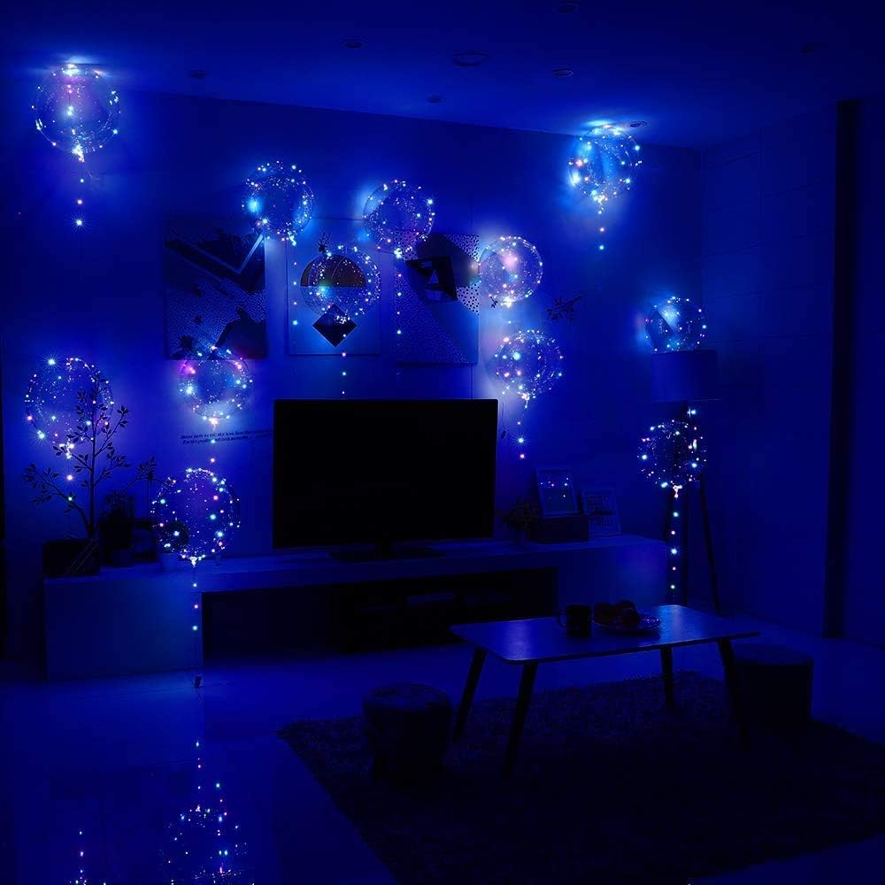 Ein Raum mit blauer Beleuchtung. Ballons mit Lichtern hängen. Es gibt einen Fernseher, einen Tisch und einen Teppich.