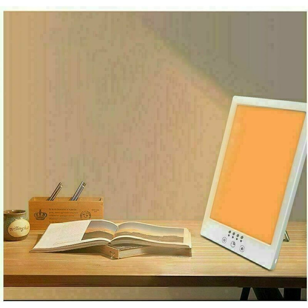 Ein Schreibtisch mit einem Buch, Stiften und einer Lichttherapielampe. Die Lampe ist an und strahlt orangefarbenes Licht aus.