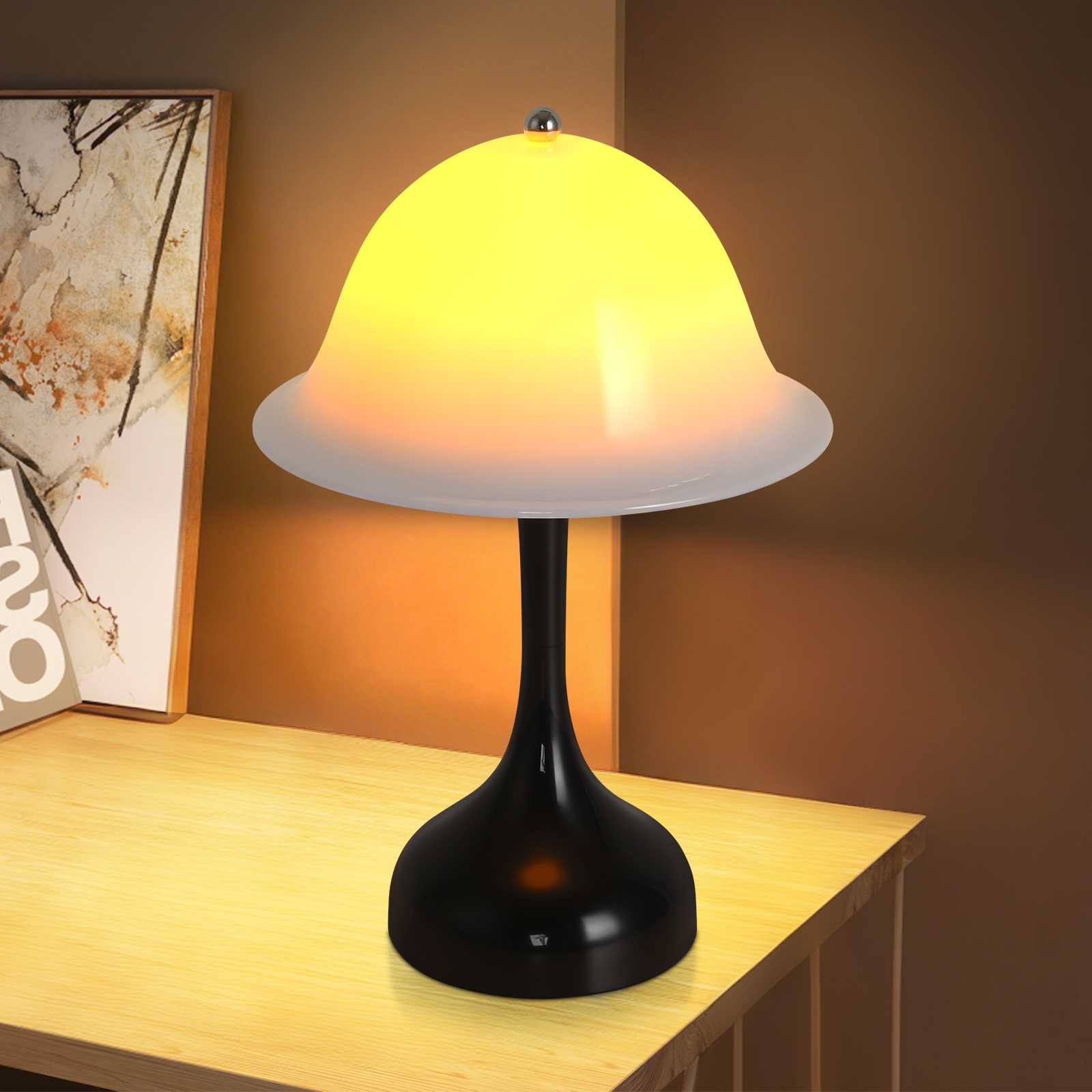 Nowoczesna lampa biurkowa z czarną podstawą i żółtym kloszem. Stoi na drewnianym biurku obok oprawionego obrazu.