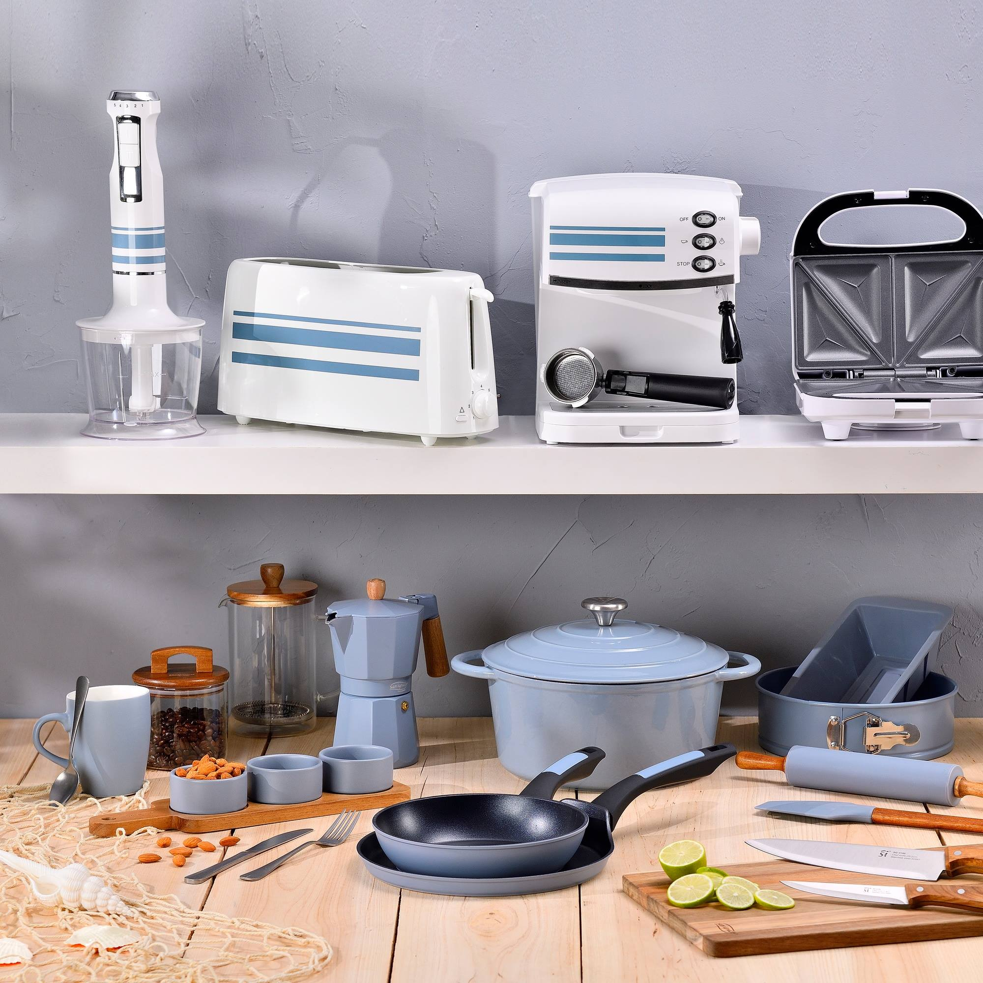 Electrodomésticos y utensilios de cocina en estantes y una mesa. Incluye una batidora, tostadora, cafetera, sandwichera y sartenes.