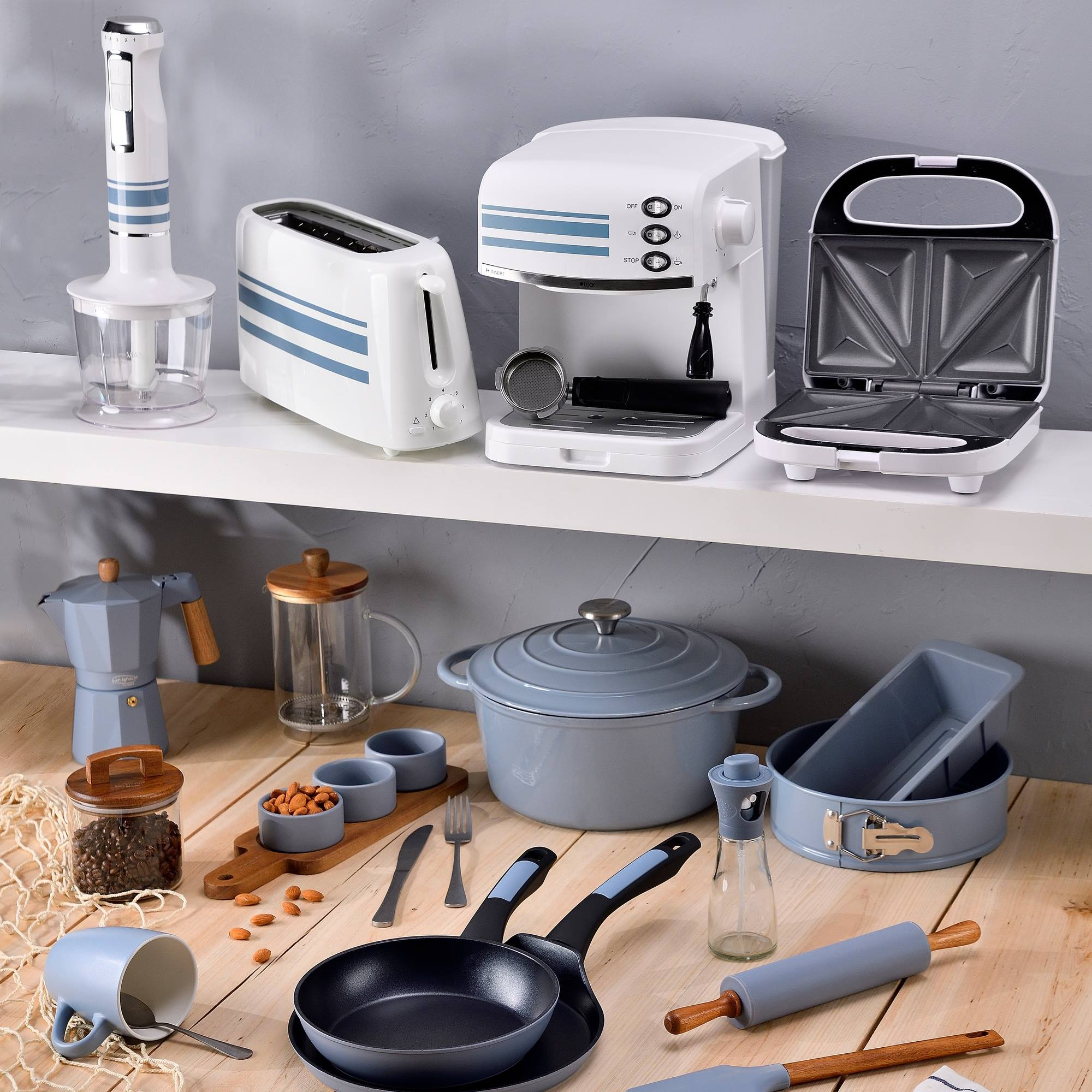 Electrodomésticos de cocina: batidora, tostadora, cafetera, sandwichera, ollas, sartenes, rodillo y alimentos en mesa de madera.
