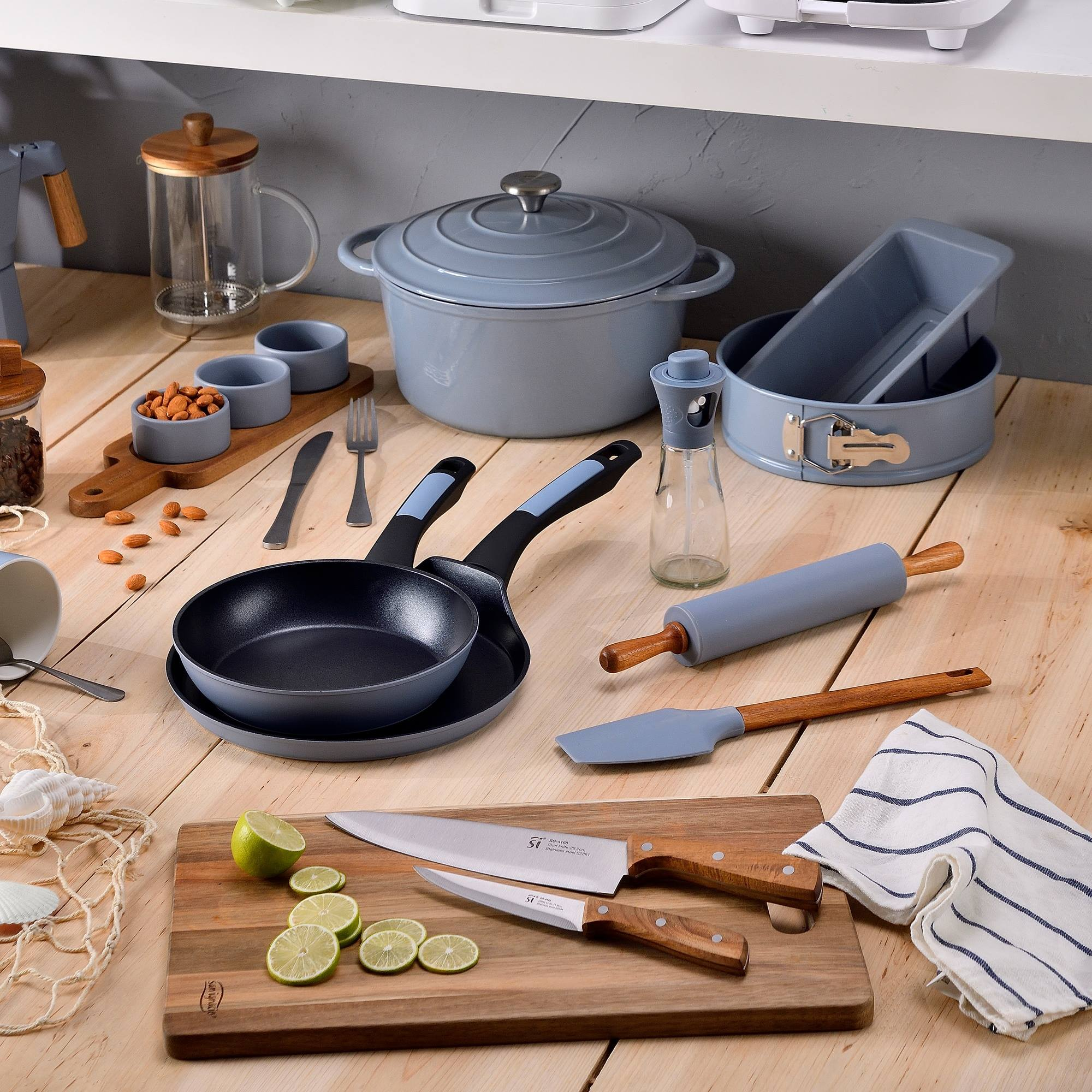 Escena de cocina con utensilios e ingredientes sobre madera. Incluye ollas, sartenes, cuchillos y limas.
