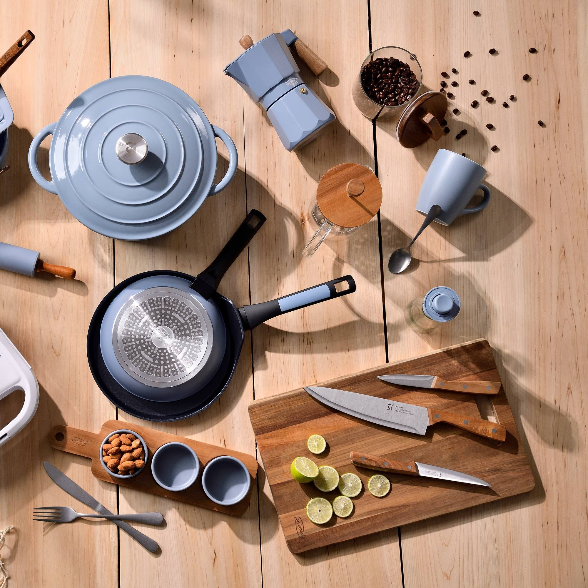 Una escena de cocina con varios utensilios de cocina azules, cuchillos, granos de café y limones sobre una superficie de madera.