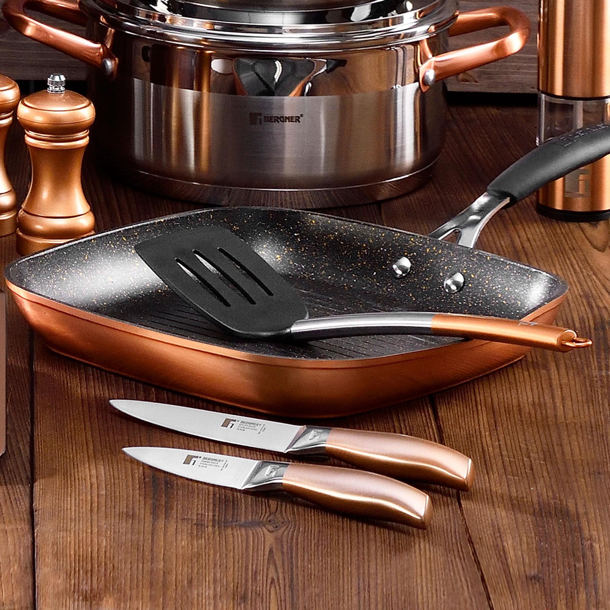Juego de utensilios de cocina: sartén, olla, cuchillos y espátula. Tonos cobre y plata sobre madera.