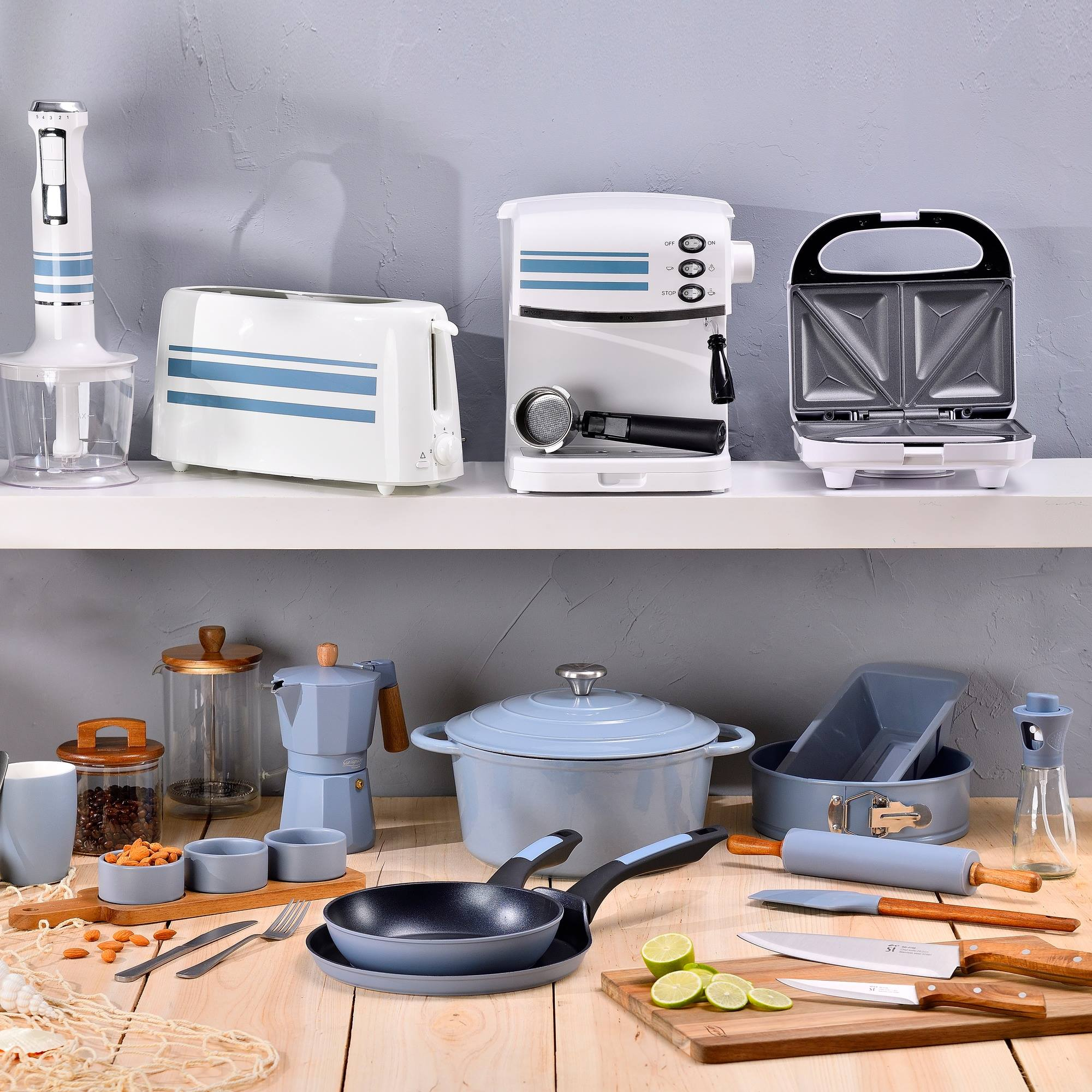 Electrodomésticos y utensilios de cocina sobre una mesa de madera. Incluye licuadora, tostadora, cafetera y sandwichera.