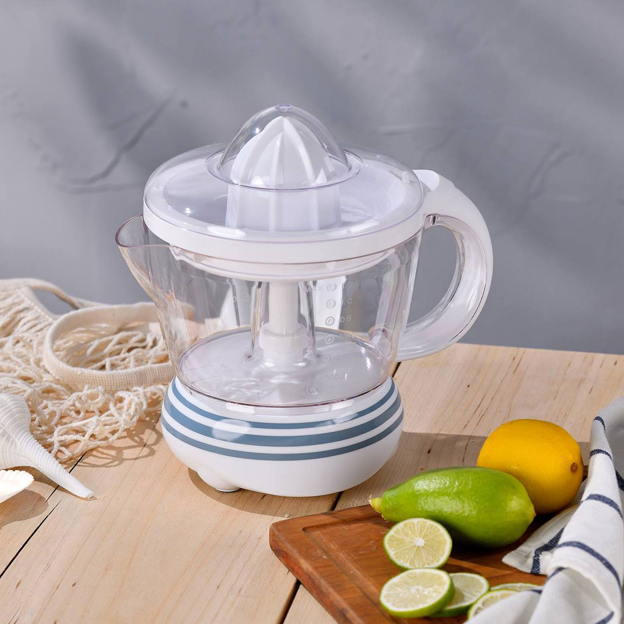 Un exprimidor blanco y transparente con limones y limas en una tabla de madera. Una concha y una bolsa de red.