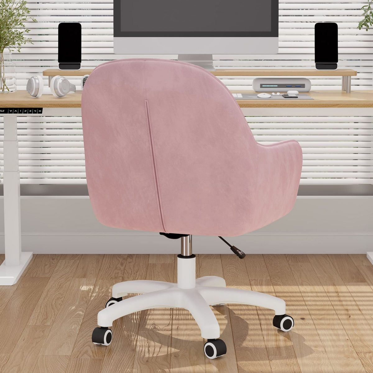Una silla de oficina rosa de espaldas al espectador. Detrás, un escritorio con monitor y accesorios. Suelo de madera.