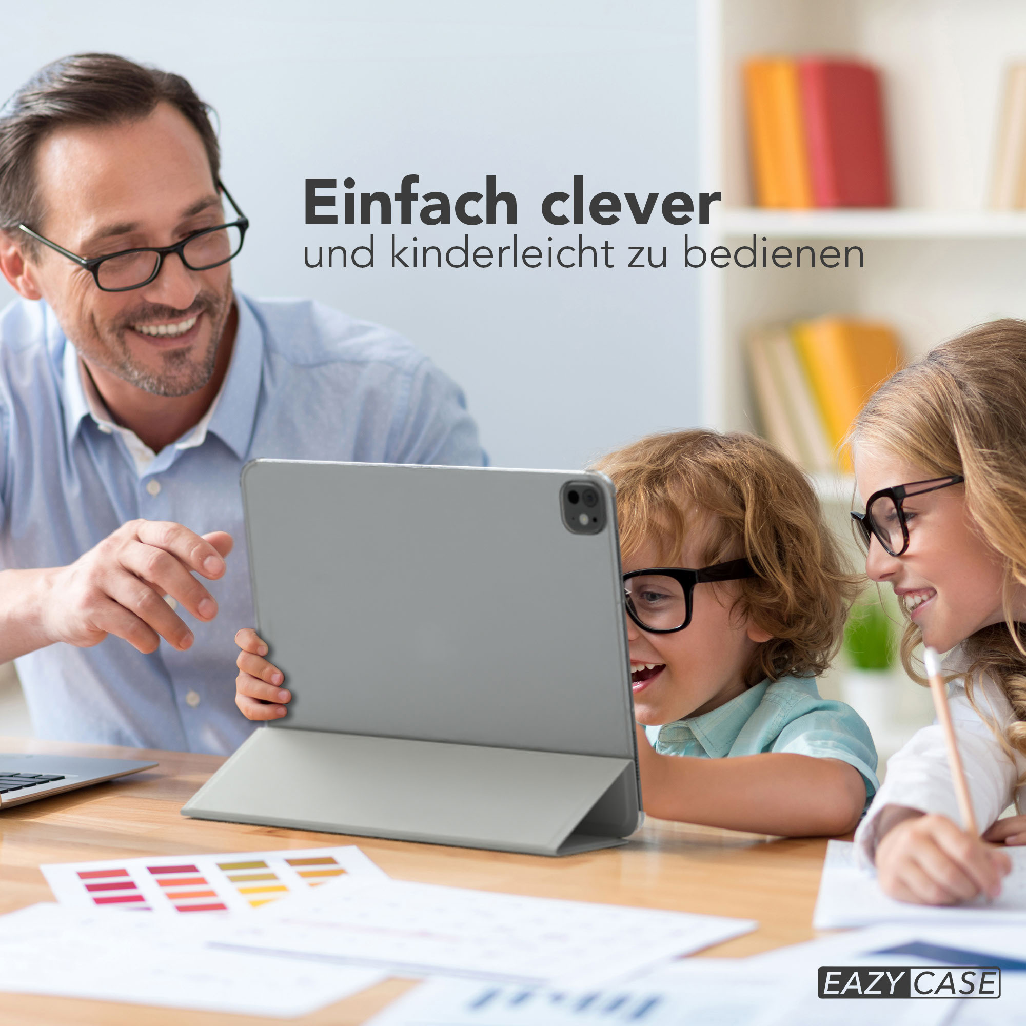 Ein Mann und zwei Kinder schauen auf ein Tablet. Die Kinder tragen Brillen und lächeln. Auf dem Tisch liegt eine Farbpalette.