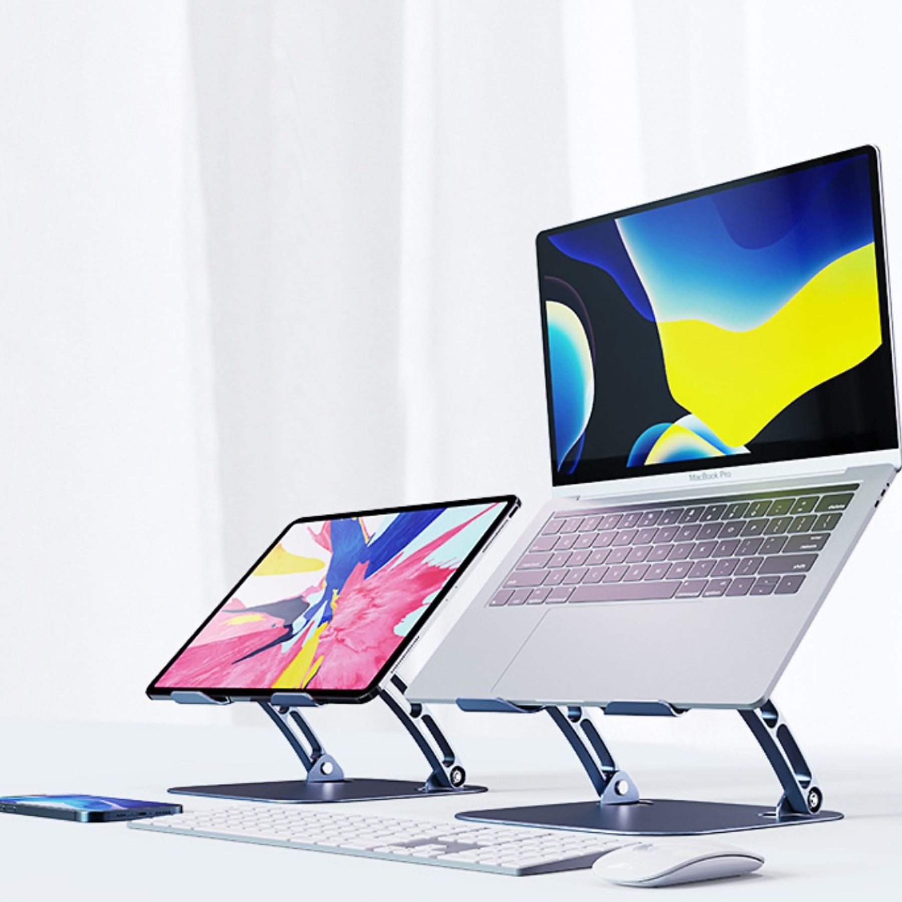 Ein Laptop und ein Tablet stehen auf Ständern. Auf dem Tisch befinden sich auch eine Tastatur, eine Maus und ein Telefon, alles in weißer Umgebung.