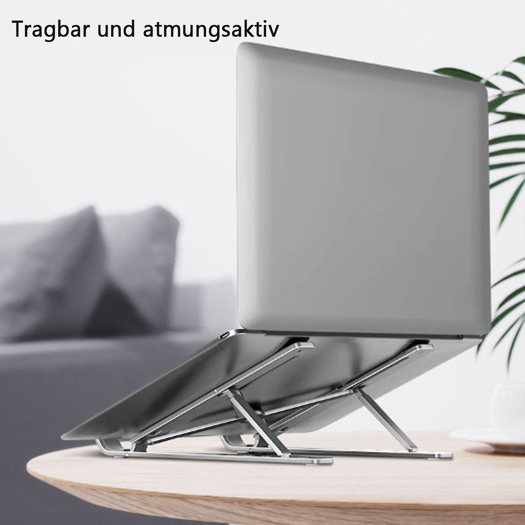 Ein Laptop steht auf einem silbernen Ständer auf einem Holztisch. Eine weiße Tasse und eine Pflanze sind im Hintergrund.