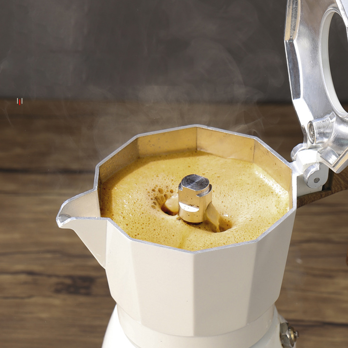 Eine weiße Mokkakanne mit brühendem Kaffee. Dampf steigt aus dem Kaffee auf. Die Kanne steht auf einer Holzoberfläche, mit dunklem Hintergrund.