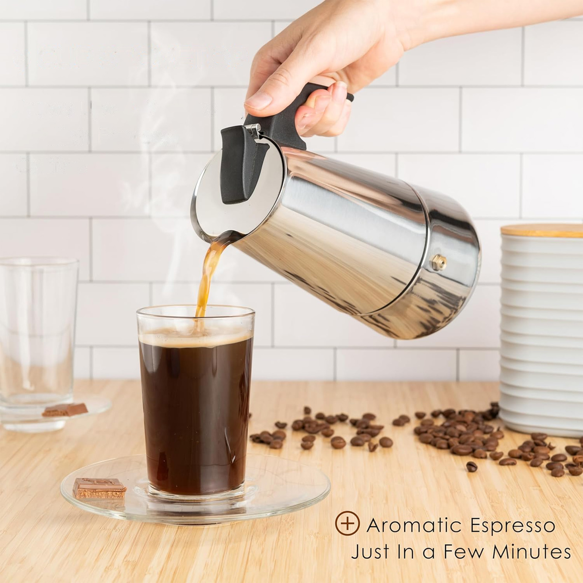 Eine Hand gießt Espresso aus einem silbernen Topf in ein Glas. Kaffeebohnen, ein Glas und ein Glas sind auf einer Holzoberfläche.
