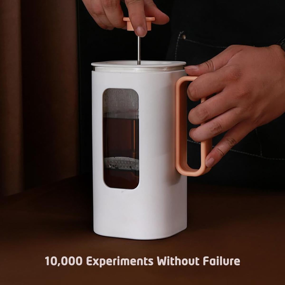 Eine Person drückt eine French Press mit Tee. Die Presse ist weiß mit einem orangefarbenen Griff. Hände sind sichtbar.