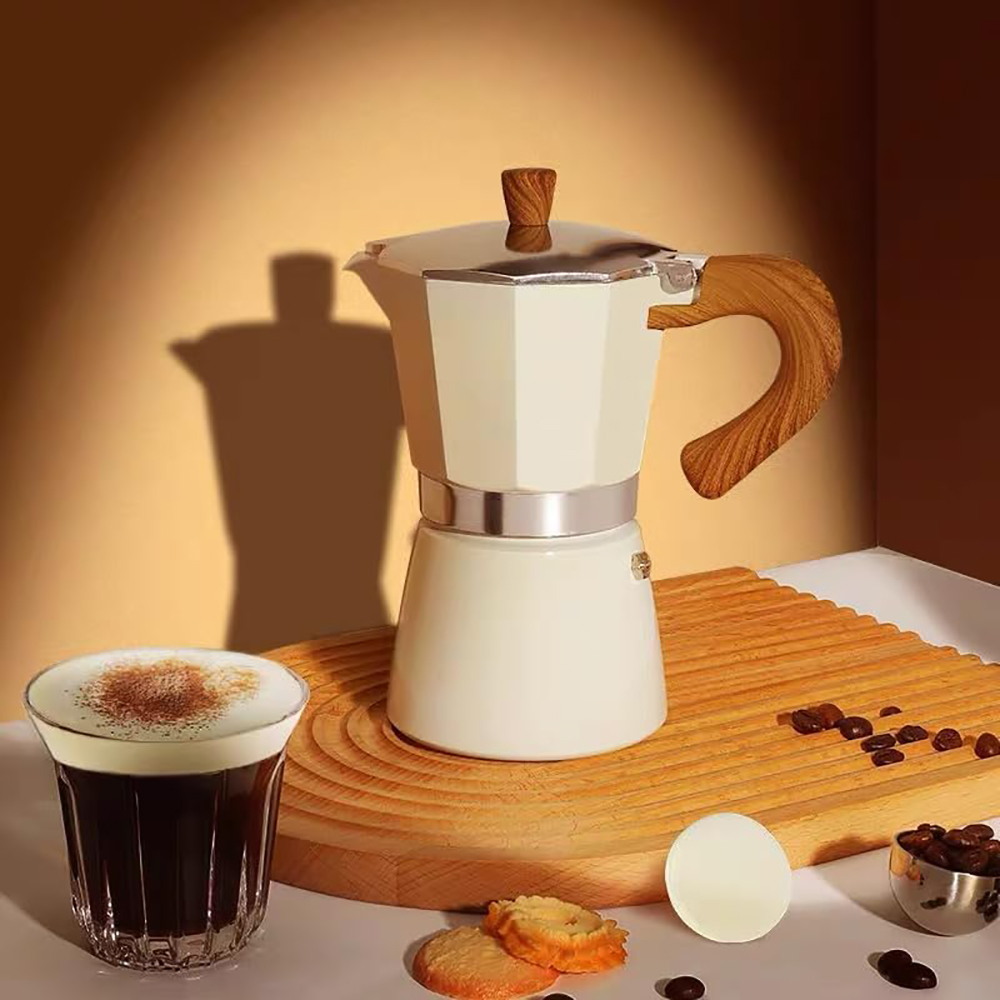 Eine cremefarbene Mokakanne mit Holzgriff steht auf einem Holzbrett. Ein Glas Kaffee, Kekse und Kaffeebohnen sind ebenfalls auf dem Tisch.