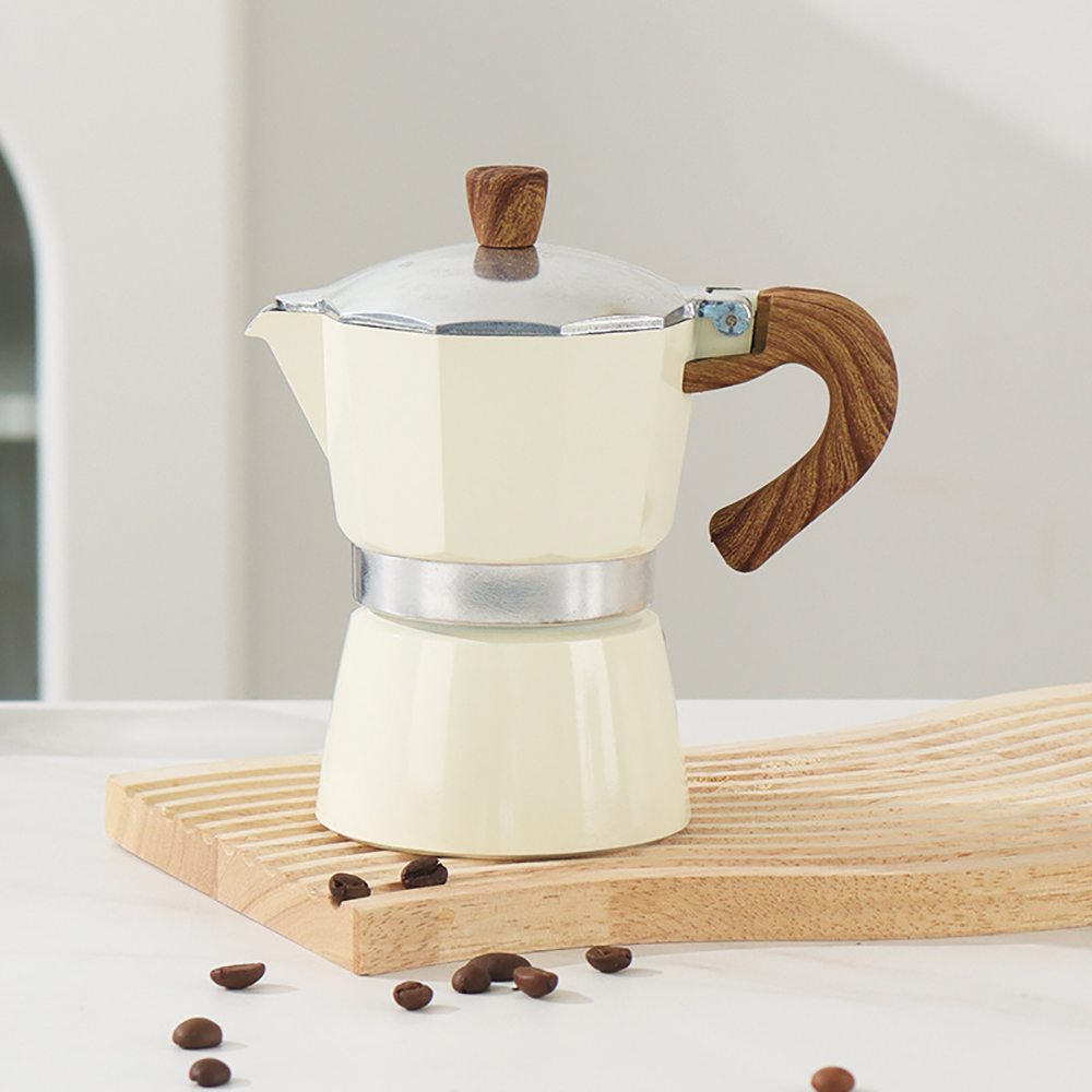 Eine cremefarbene Kaffeemaschine mit Holzgriff und -deckel. Sie steht auf einem Holzbrett. Kaffeebohnen sind verstreut.