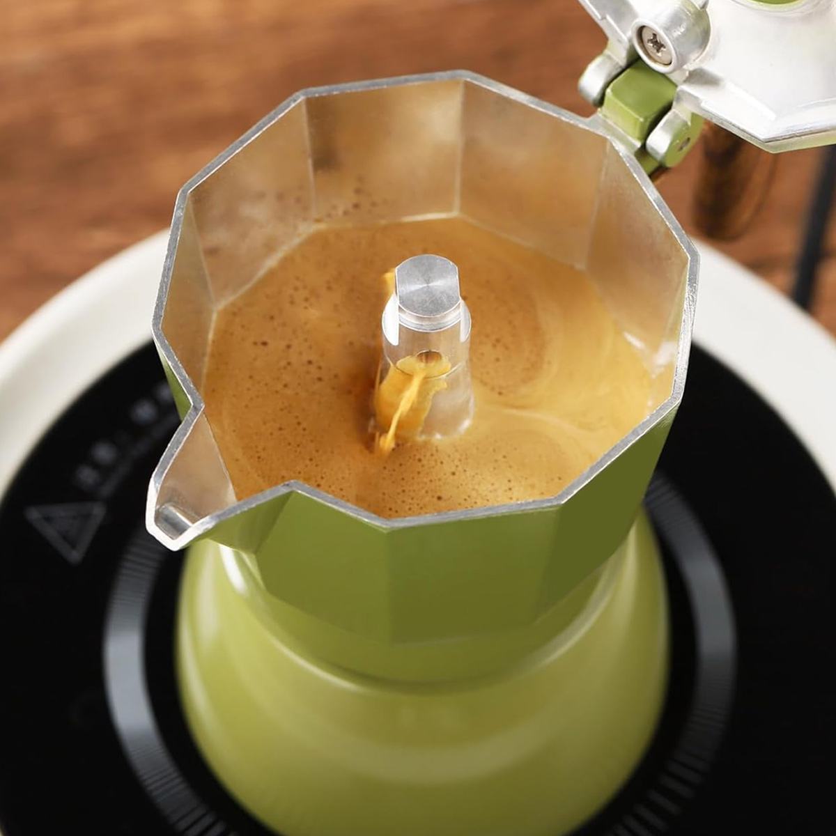 Eine grüne Espressokanne auf einem schwarzen Herd brüht Kaffee. Der Kaffee fließt in die obere Kammer.