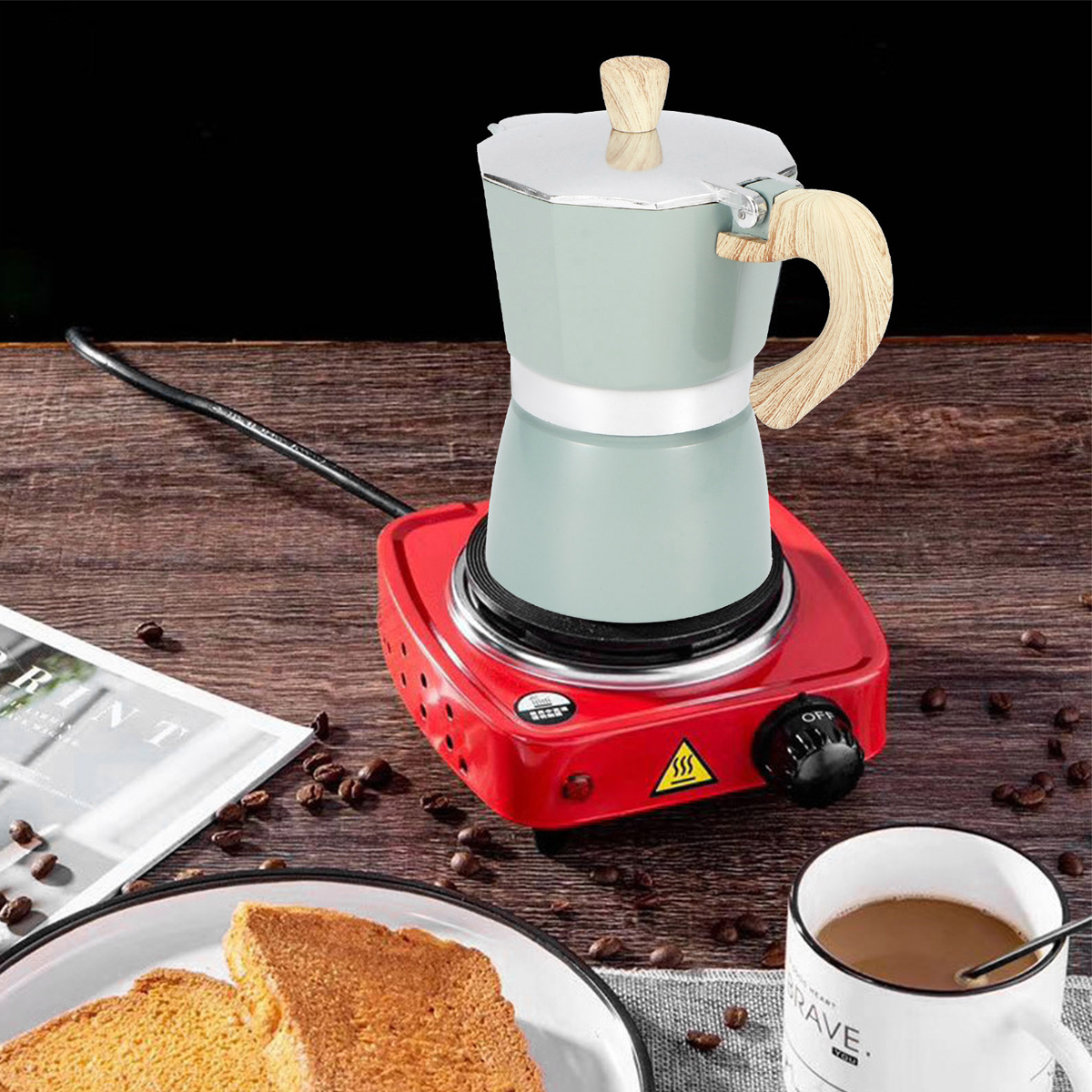 Eine Kaffeemaschine steht auf einer roten Herdplatte. Toast, Kaffee und Bohnen liegen auf einem Holztisch. Eine Zeitschrift ist in der Nähe.