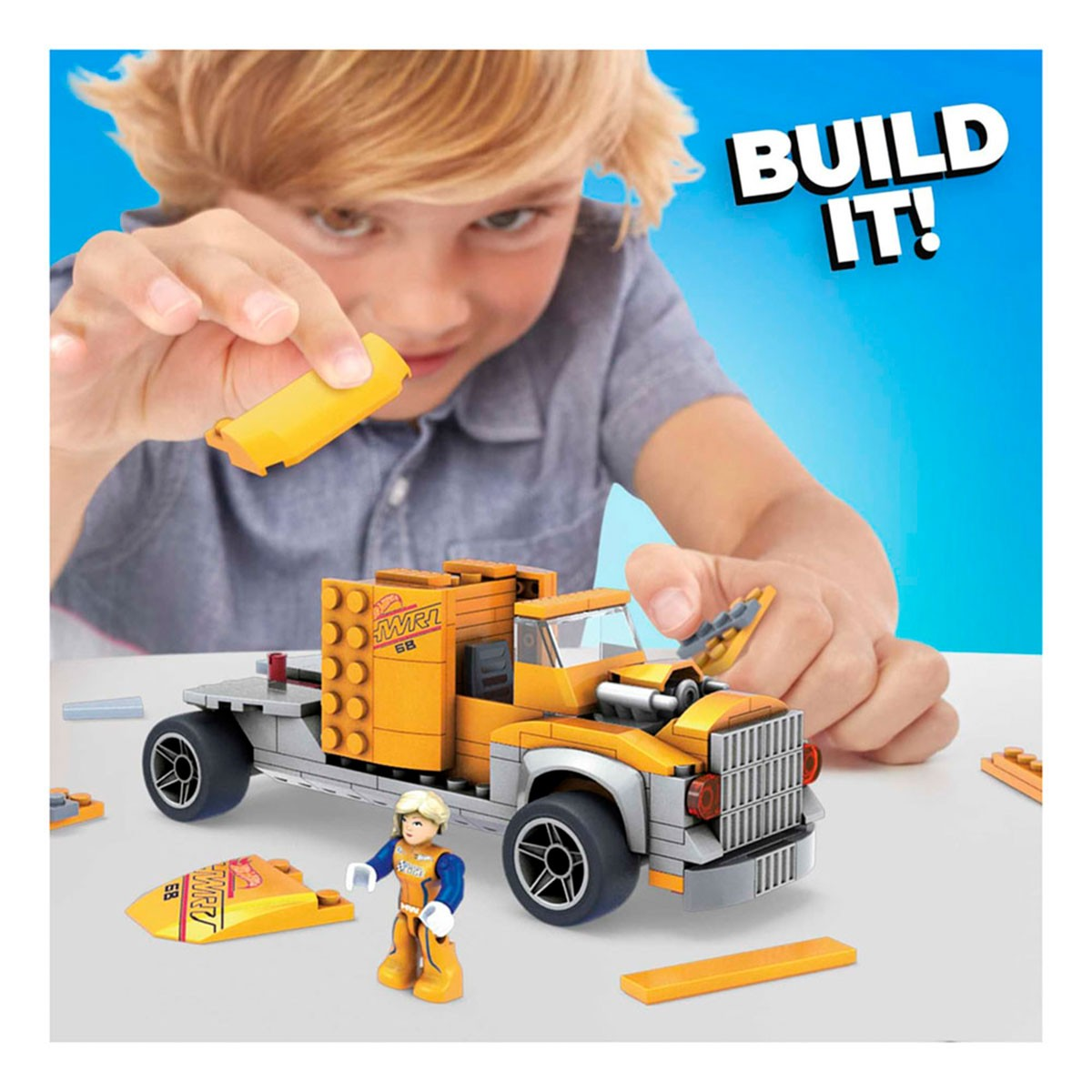 Ein Kind baut einen Spielzeug-LKW. Der LKW ist gelb und grau mit schwarzen Rädern. Eine kleine Figur und lose Teile liegen auf dem Tisch.