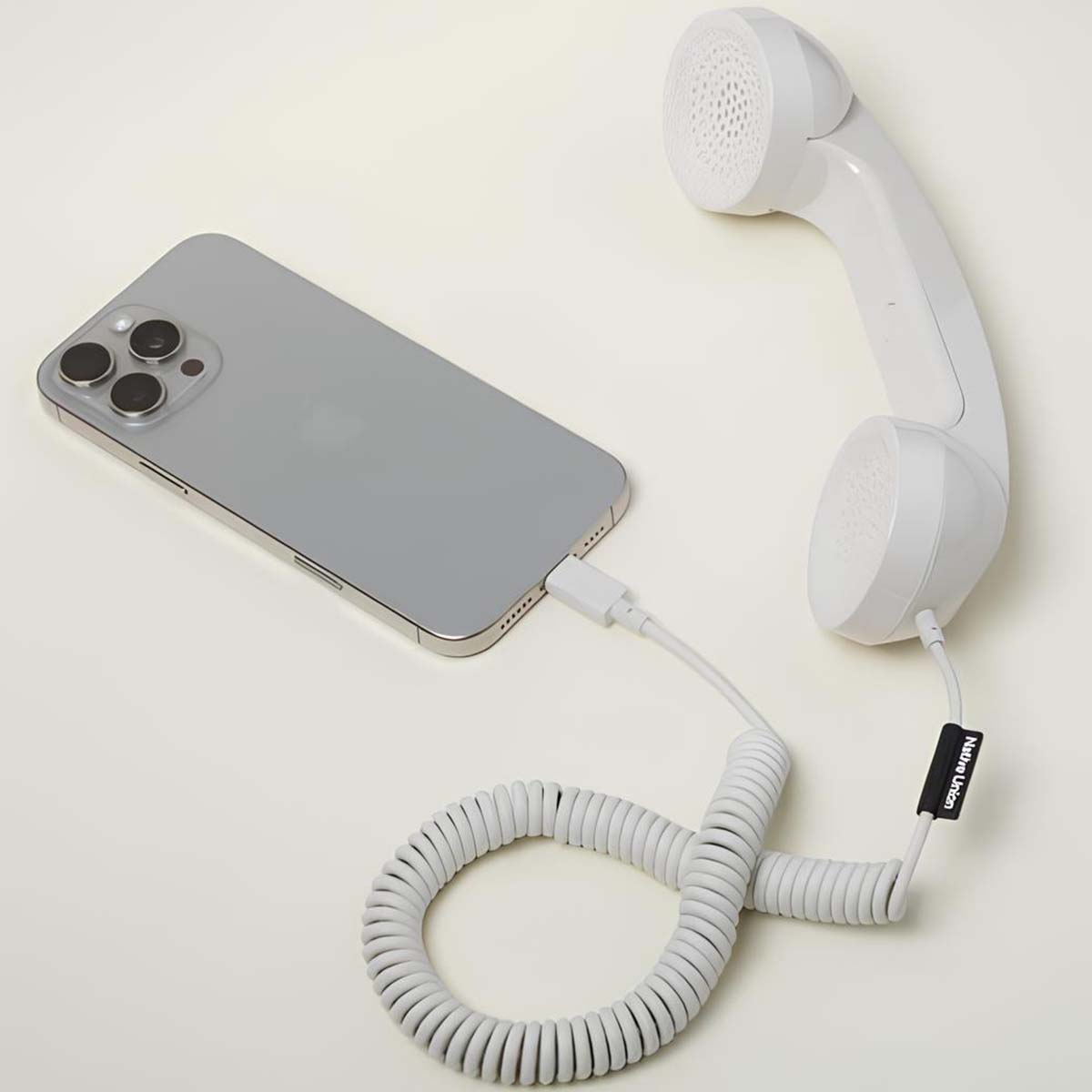 Una cornetta bianca collegata a un iPhone grigio tramite un cavo bianco. La cornetta è su una superficie bianca.
