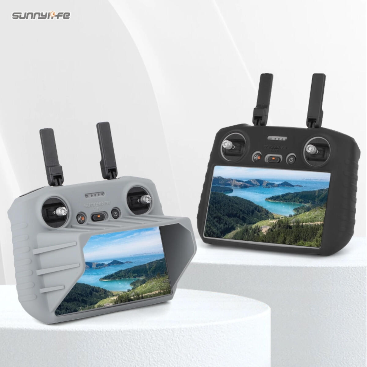 Two drone controllers with screens displaying a landscape. One grey, one black, both with antennas, sitting on a white surface.