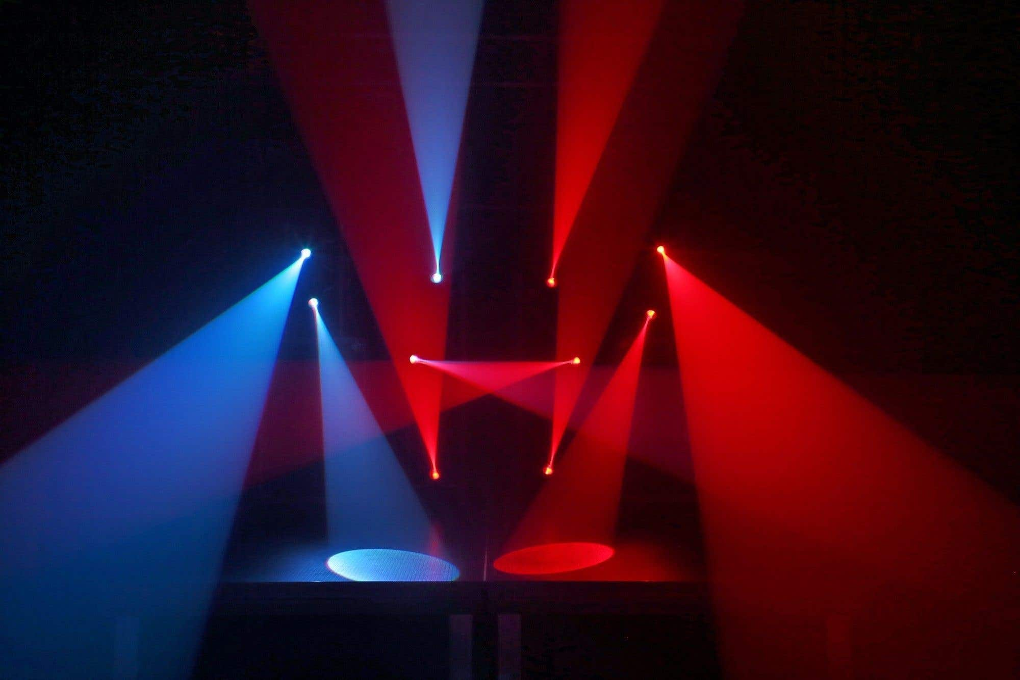 Luces de escenario proyectan haces rojos y azules. Los haces convergen, creando una exhibición visualmente dinámica.