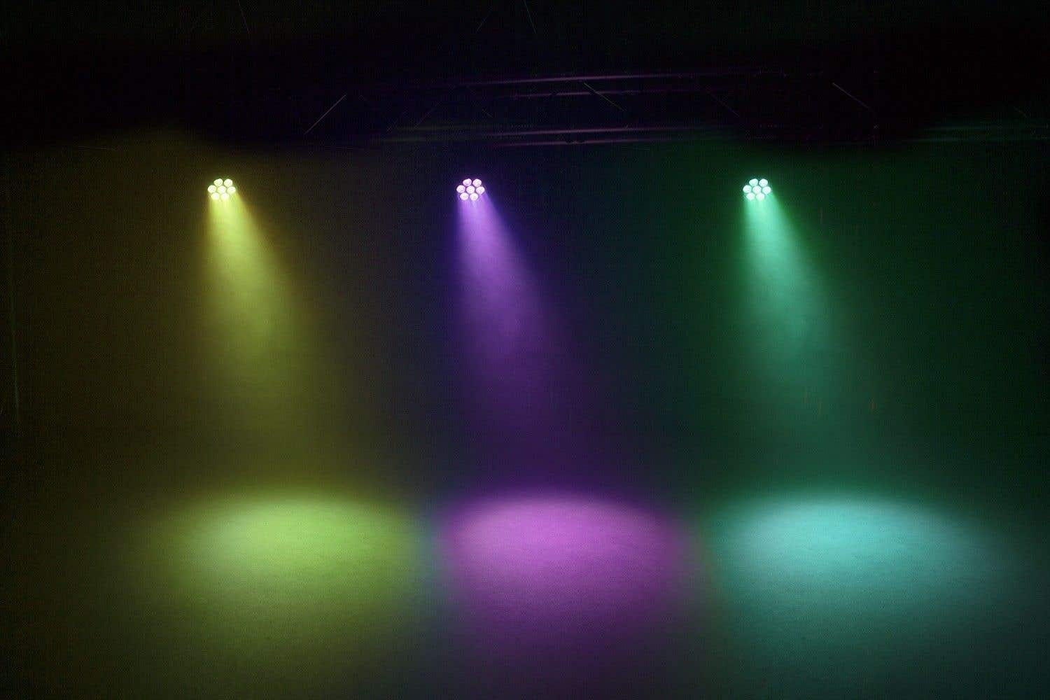 Tres focos brillan: amarillo, morado y verde. Iluminan el espacio ahumado. Las luces están en el centro superior.